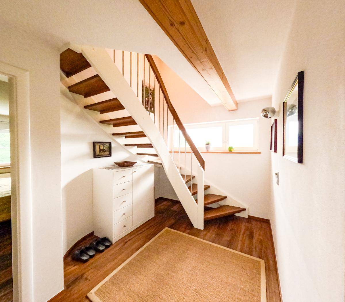 Heller Flur mit Holztreppe, Holzbalken und Parkettboden.