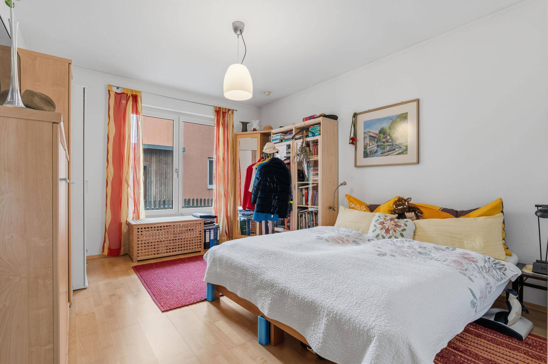 Gemütliches Schlafzimmer mit Doppelbett, Holzfußboden und Fenster mit farbigen Vorhängen.