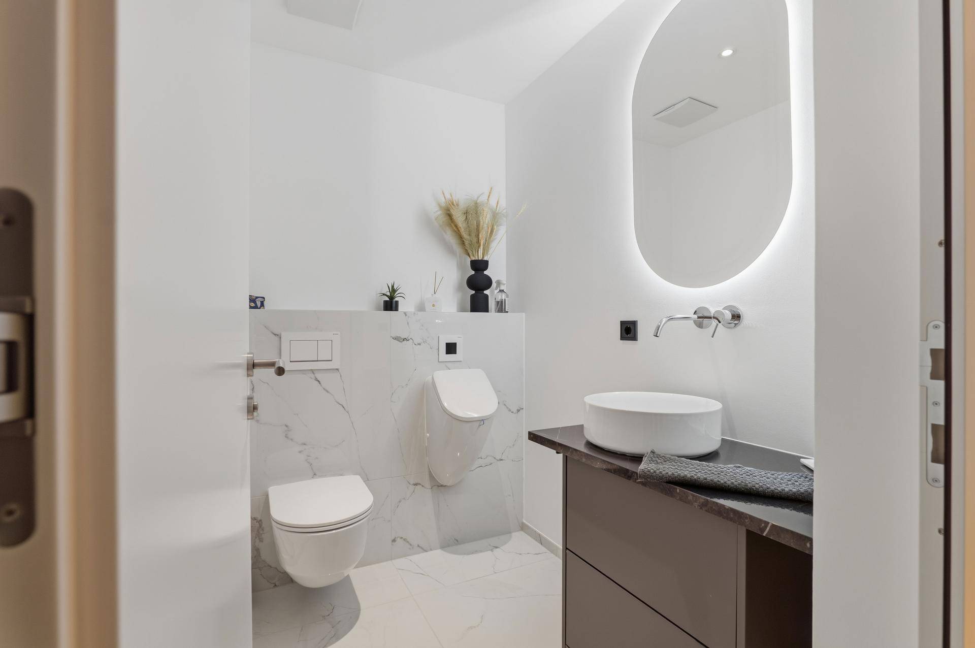 Modernes Gäste-WC mit Wand-WC, Urinal, stilvollem Waschbecken und Marmoroptik-Fliesen.