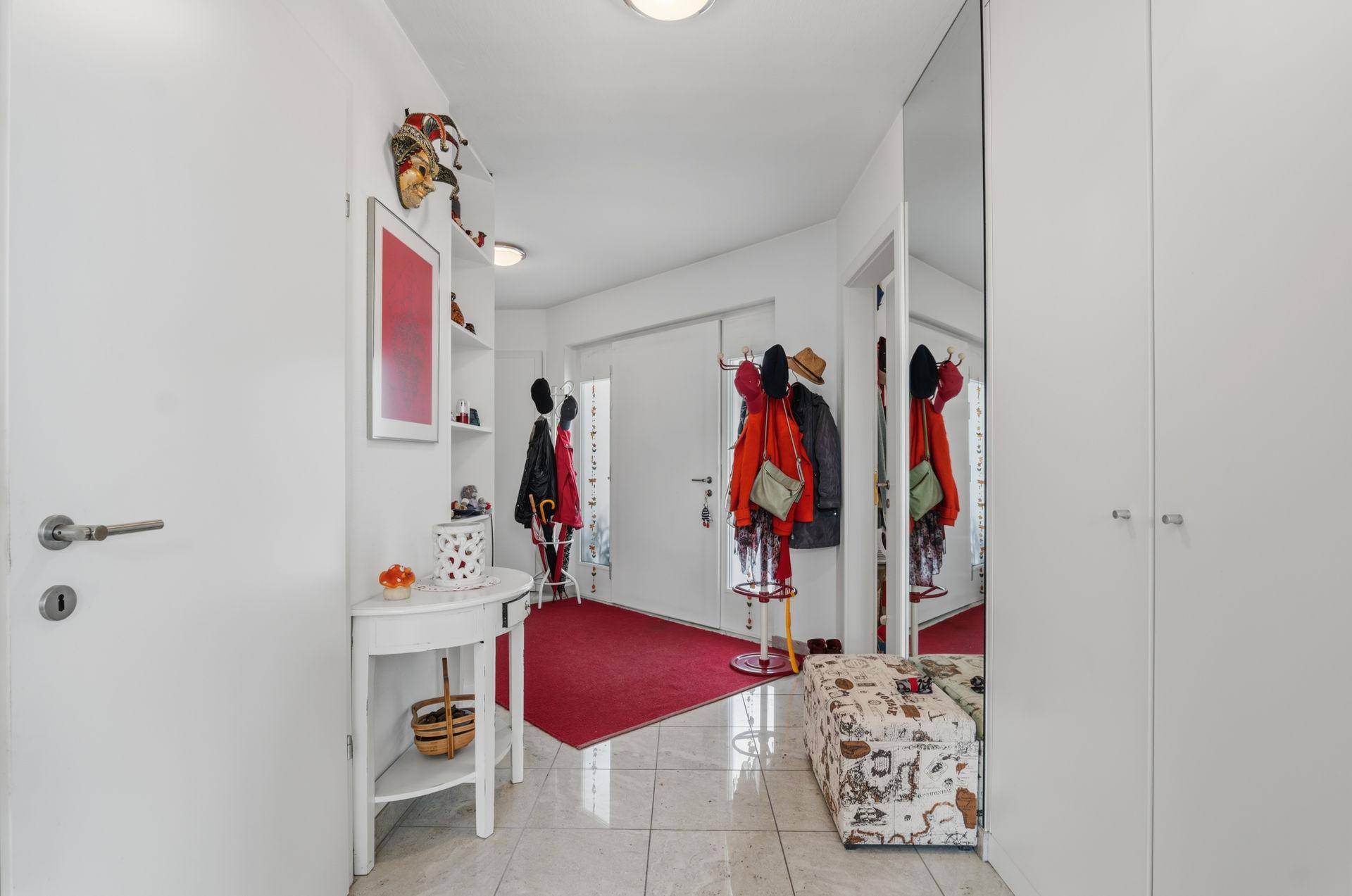 Heller Eingangsbereich mit Fliesenboden, großem Spiegel und Garderobe.