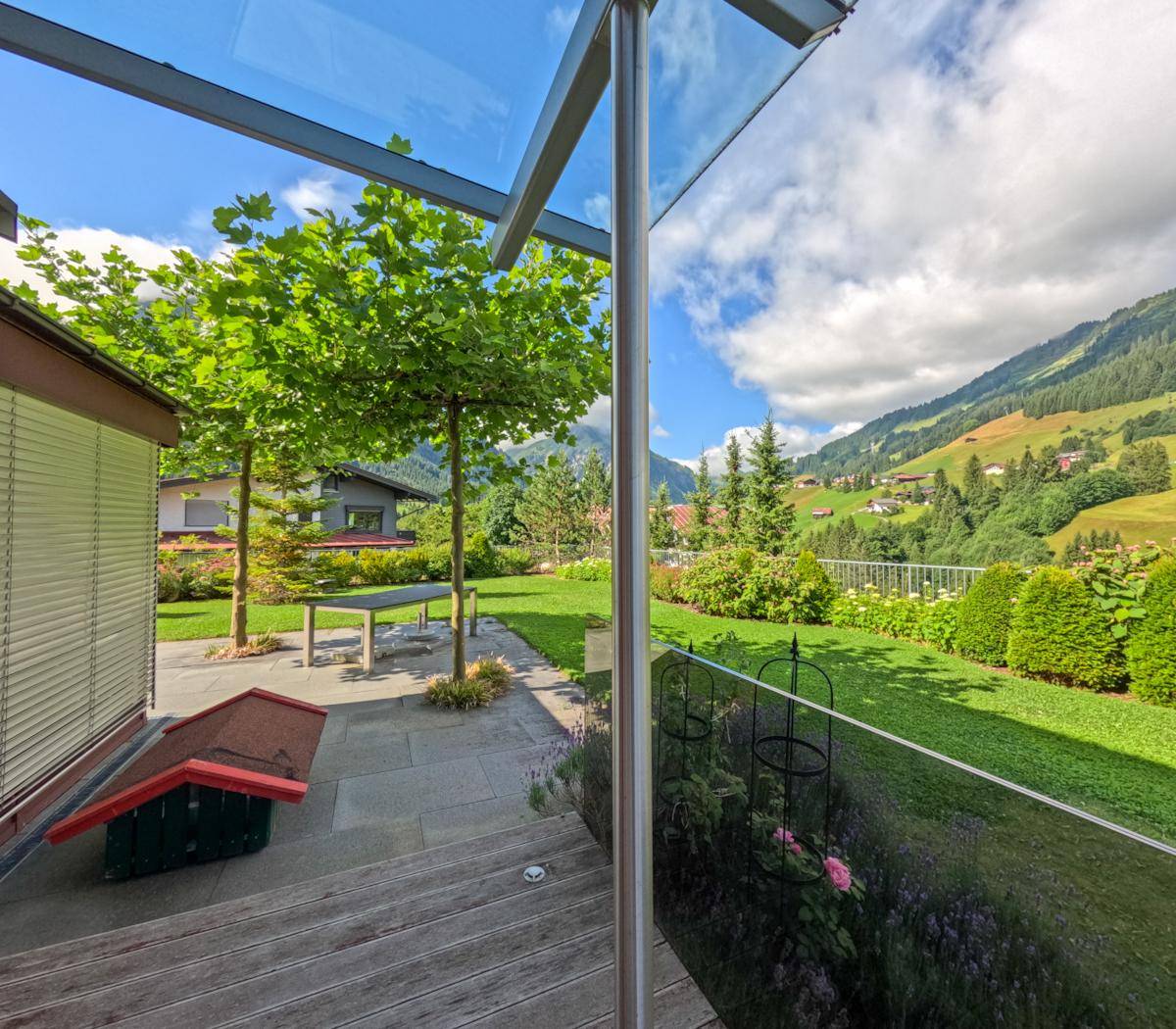 Holzterrasse mit Glasüberdachung und Panoramablick auf die grüne Berglandschaft.