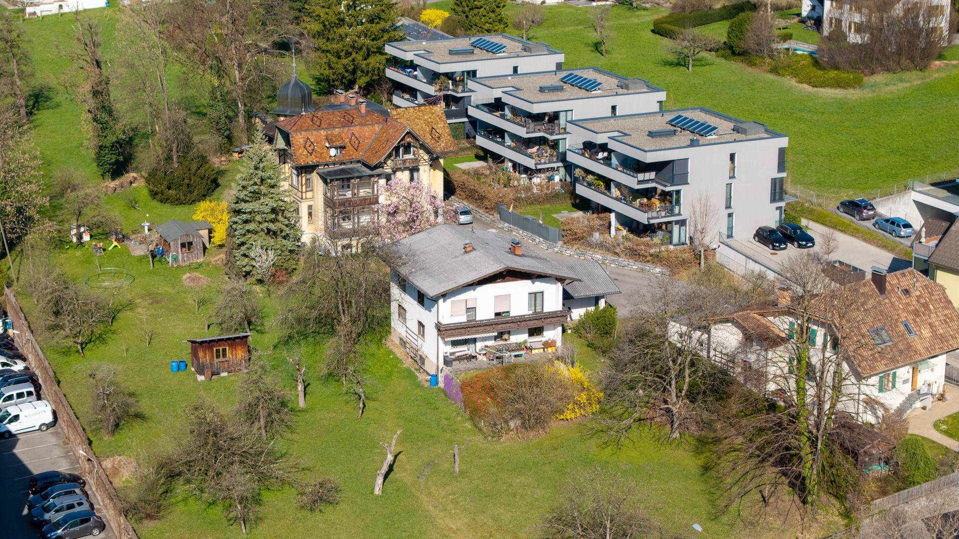 Luftaufnahme eines Wohngebiets mit verschiedenen Gebäudetypen, Gärten und Bäumen.