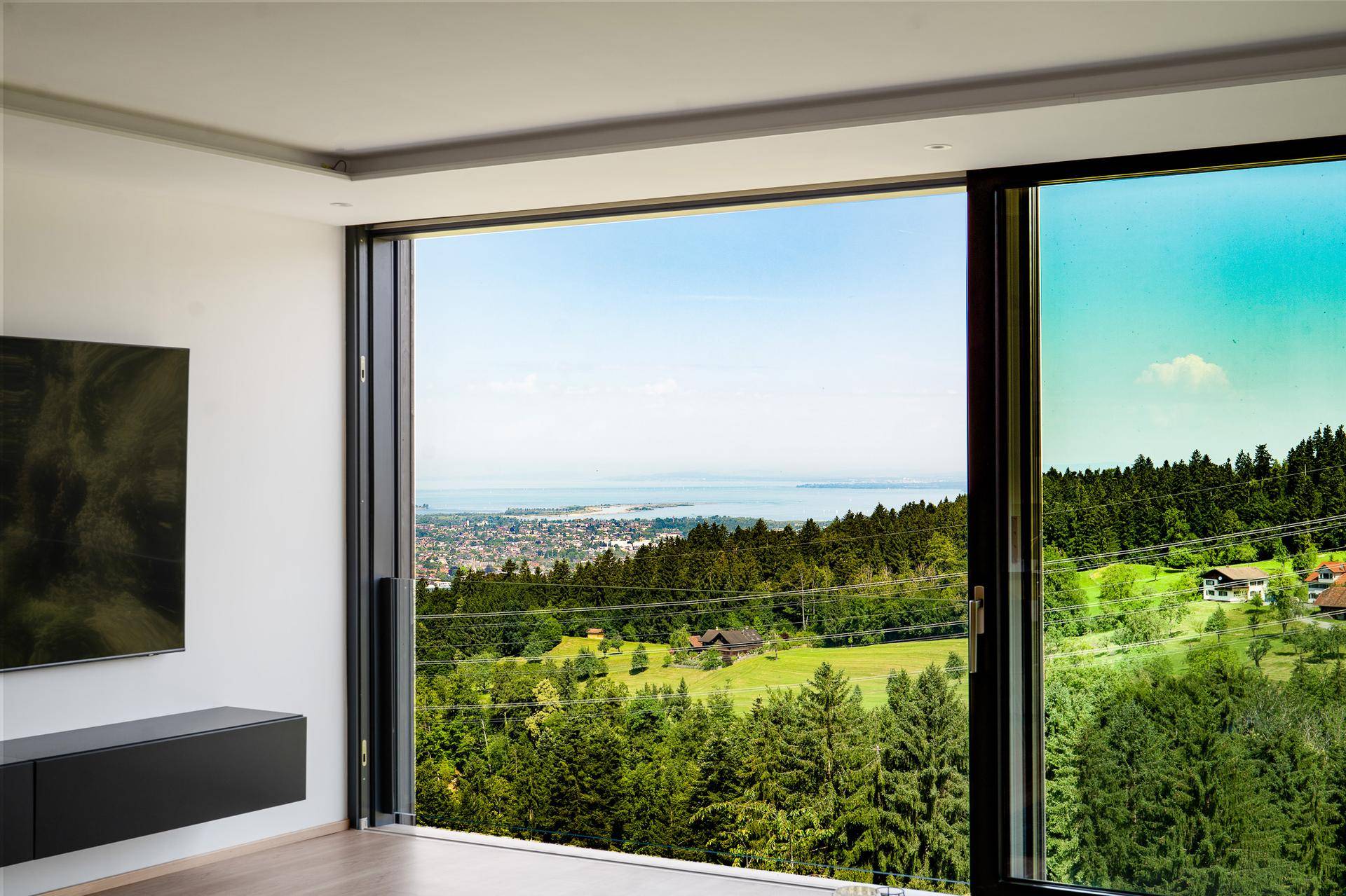 Heller Wohnraum mit großen Schiebetüren und beeindruckendem Ausblick auf den See und die umliegende Natur.