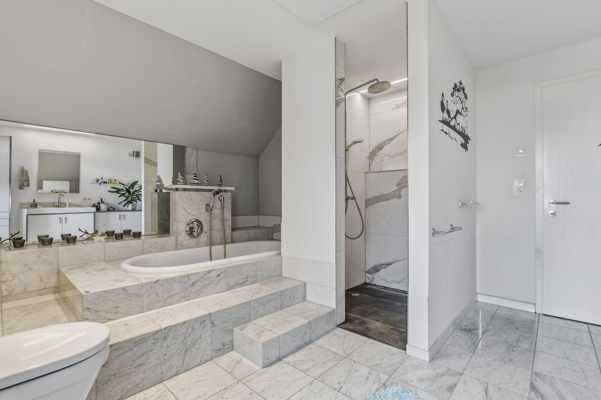 Luxuriöses Badezimmer mit Marmorfliesen, eingelassener Badewanne und begehbarer Dusche, sehr elegant.