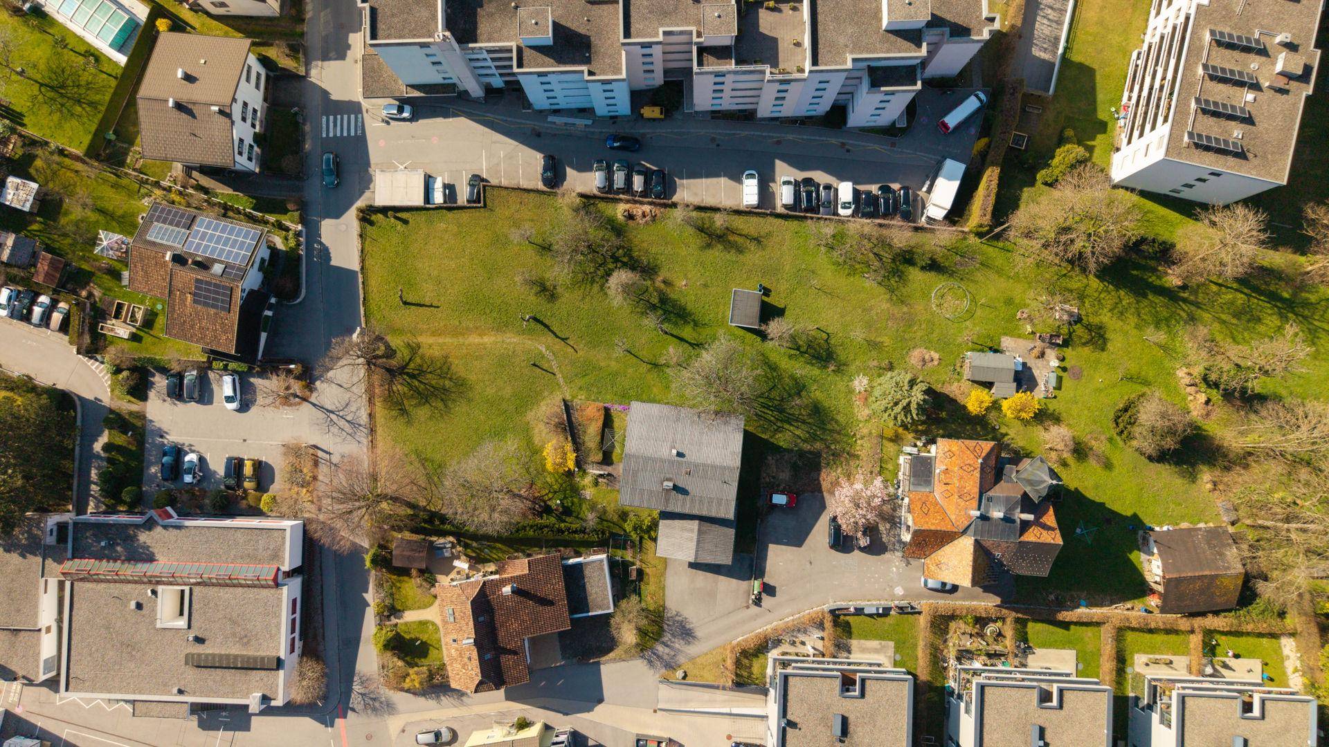 Luftbild eines umrandeten Grundstücks mit Rasenfläche, umgeben von Gebäuden und Parkplätzen.