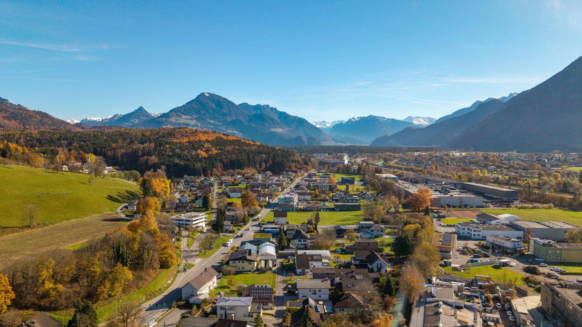 Malerische Luftaufnahme einer Siedlung umgeben von Bergen und herbstlichen Wäldern, weite Aussicht.