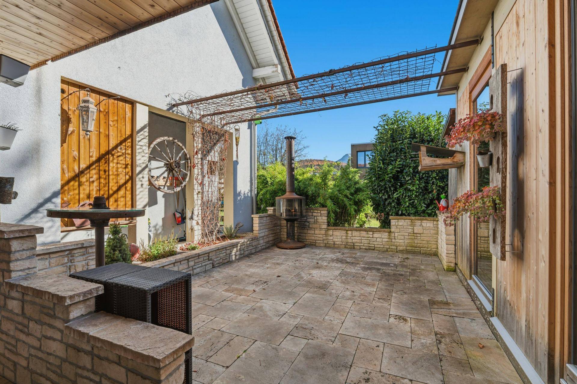 Gemütliche Steinterrasse mit Außenkamin, Sitzgelegenheiten und Pergola für entspannte Stunden im Freien.