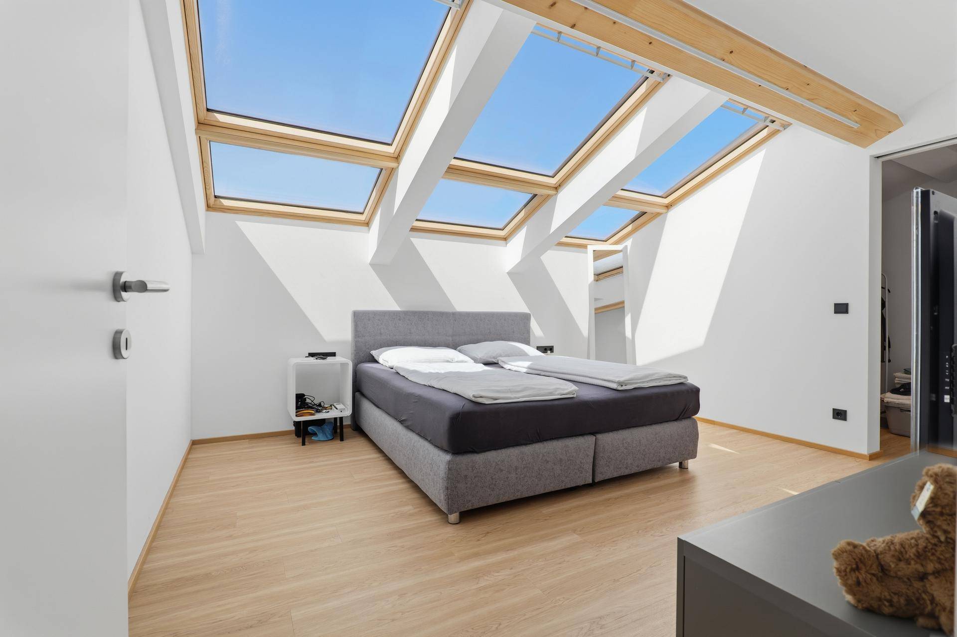 Helles Schlafzimmer im Dachgeschoss mit mehreren Dachfenstern, Holzbalken und Doppelbett.