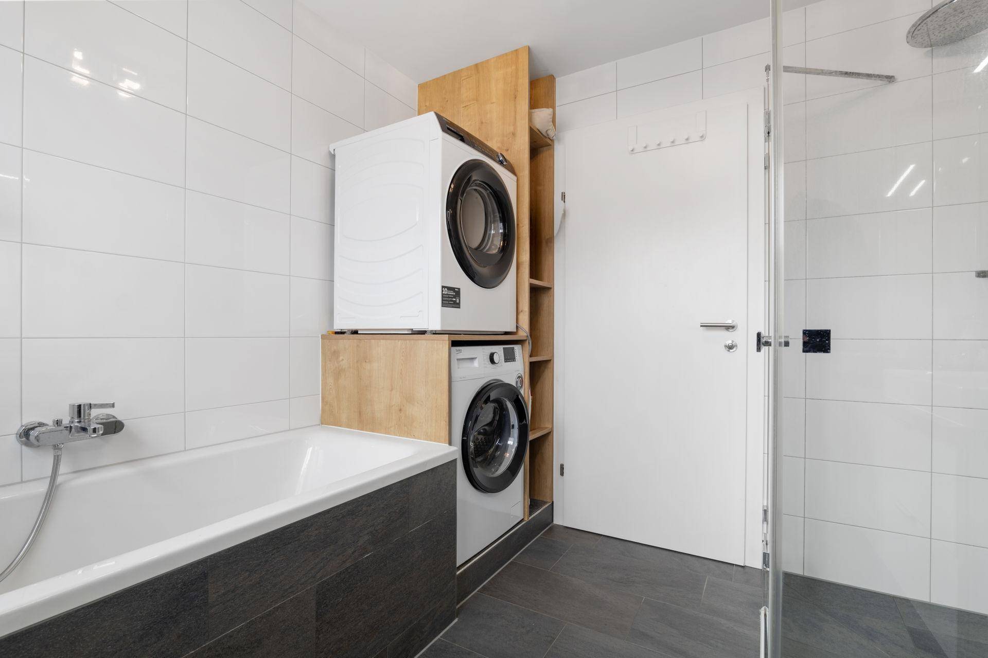 Modernes Badezimmer mit Badewanne, integrierter Waschmaschine und Trockner in einem praktischen Holzregal.