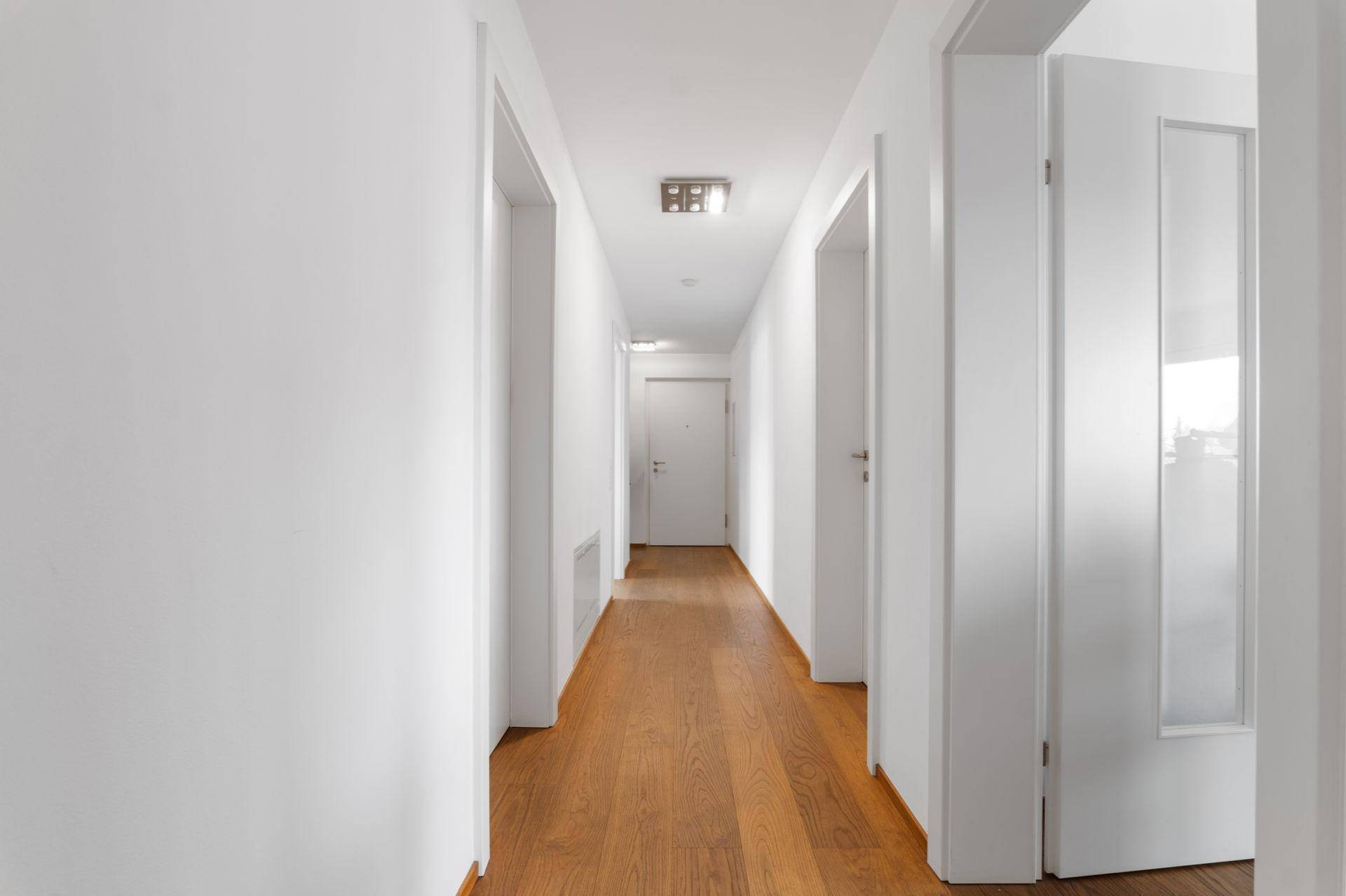 Langer, heller Flur mit Holzboden und mehreren weißen Türen, der die verschiedenen Räume verbindet.