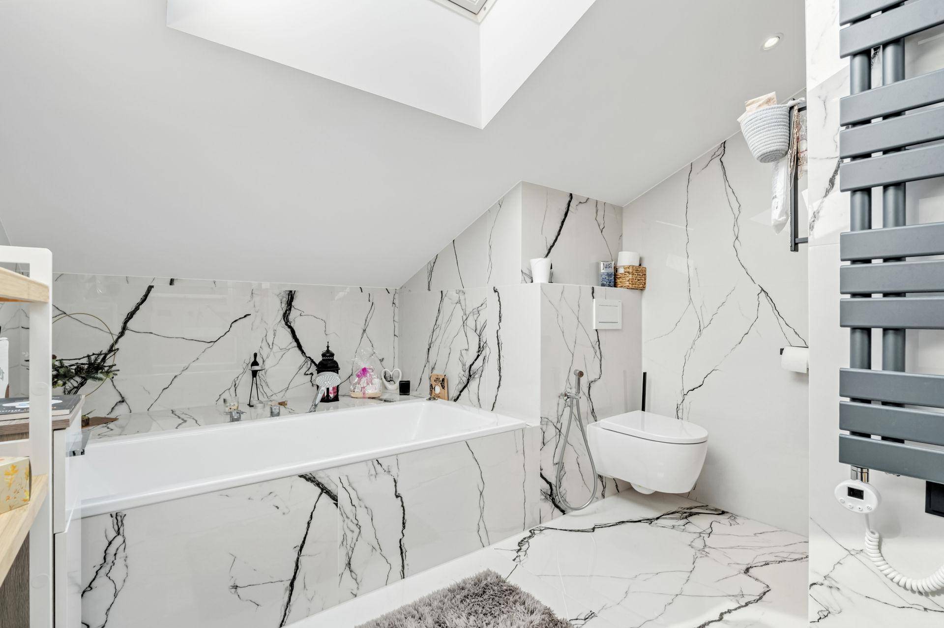 Elegantes Badezimmer mit Badewanne, wandhängendem WC und luxuriösen Marmoroptik-Fliesen.