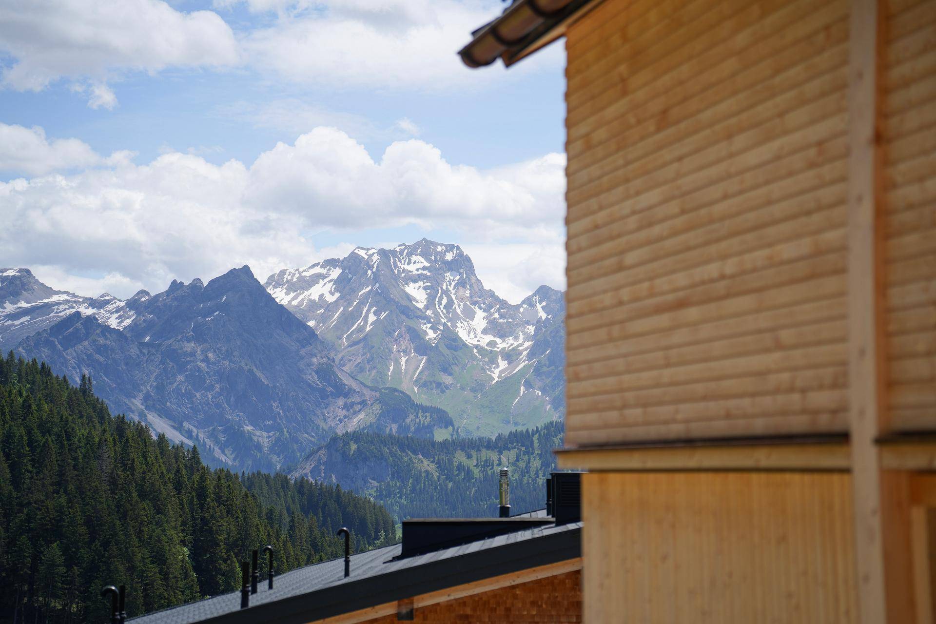 Panoramablick auf schneebedeckte Berge und grüne Wälder von einem modernen Holzhaus aus.