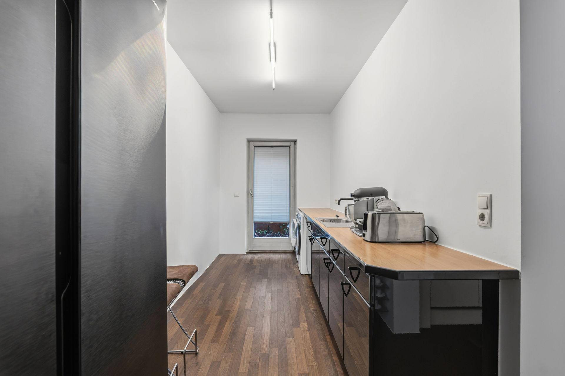 Schmaler Hauswirtschaftsraum mit Arbeitsplatte, Spüle, Waschmaschine und Zugang nach draußen.