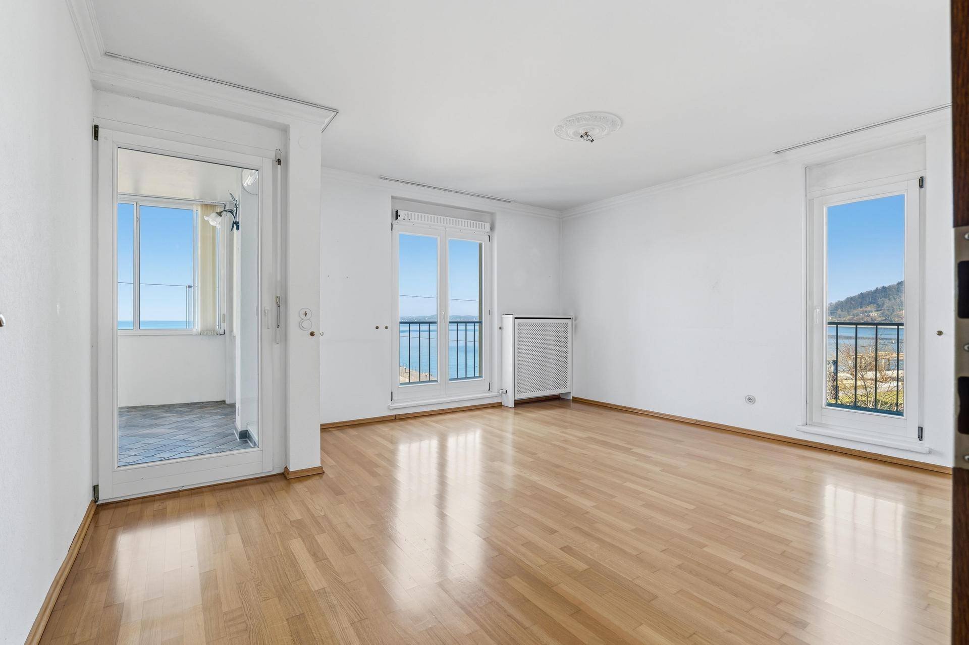 Helles Zimmer mit Parkettboden, zwei französischen Balkonen und Zugang zu einem verglasten Wintergarten mit Seeblick.