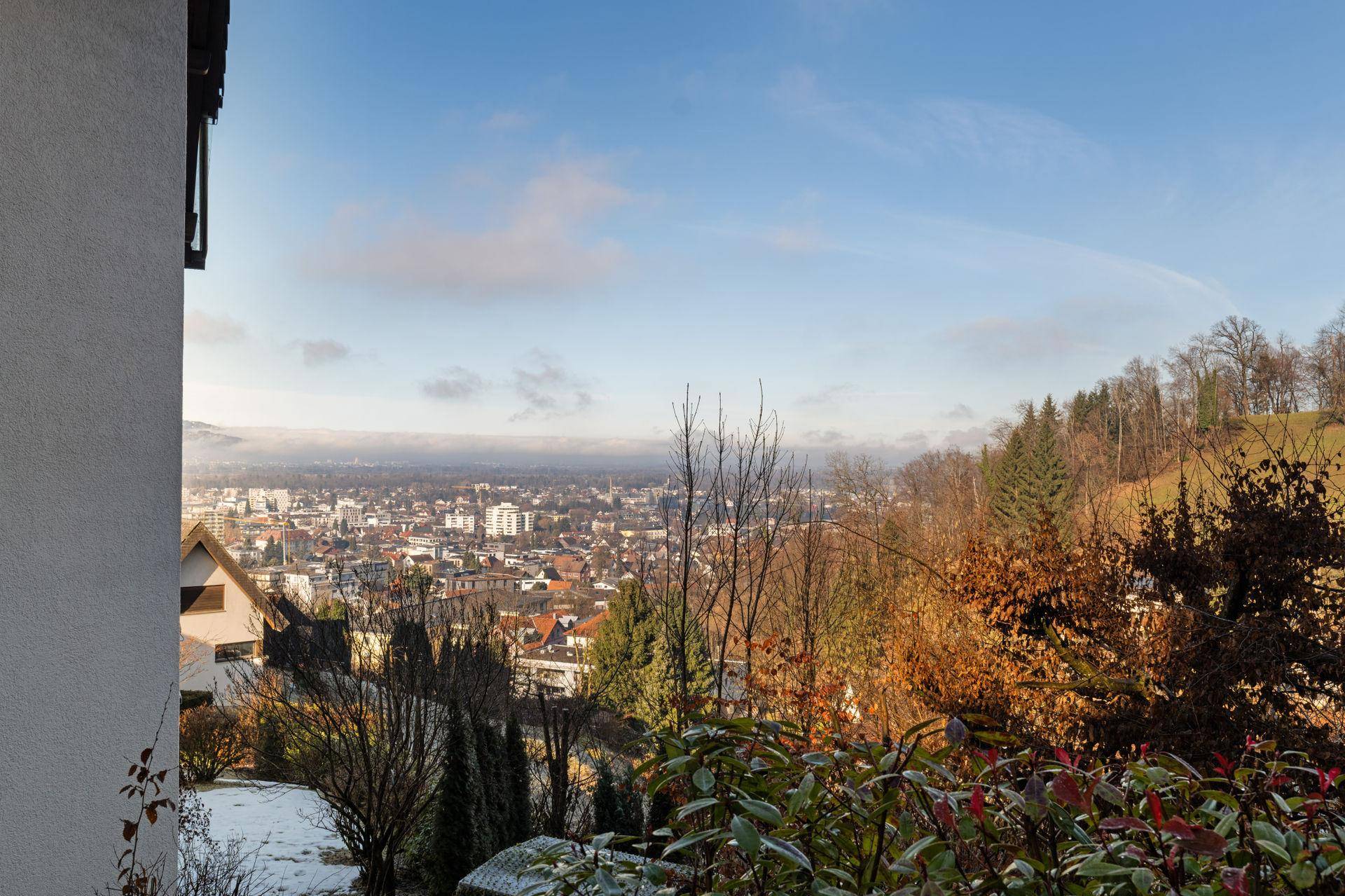Panoramablick über eine Stadt und die umliegende Hügellandschaft an einem sonnigen Wintertag.
