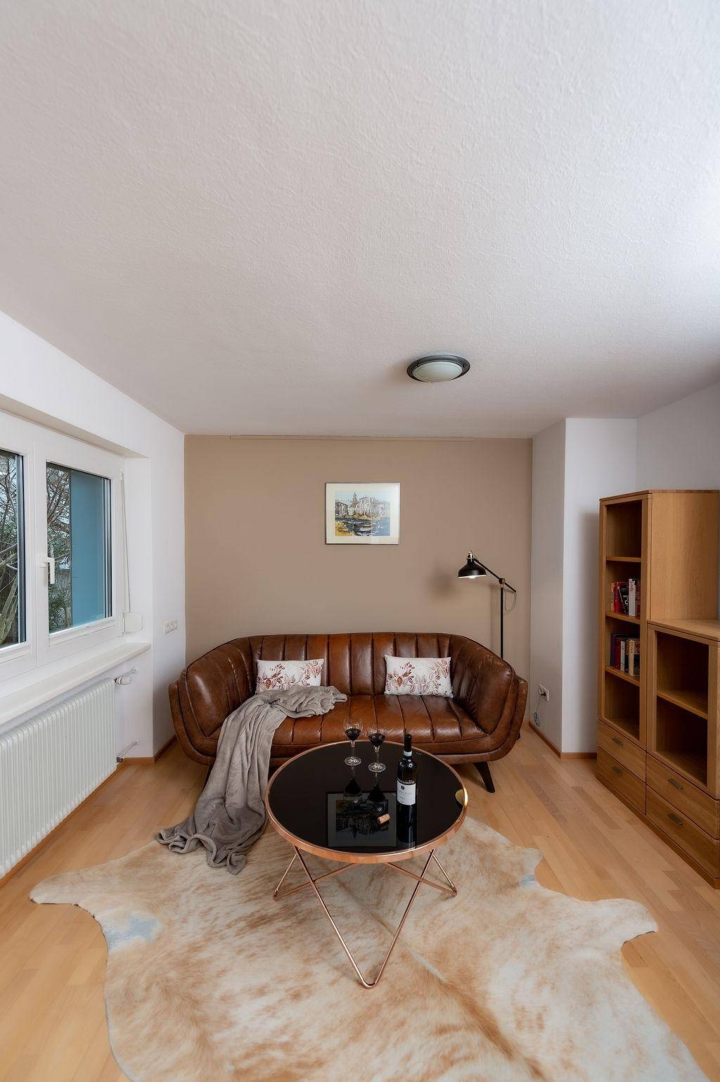 Gemütliches Wohnzimmer mit braunem Ledersofa, rundem Couchtisch und hellem Holzboden.
