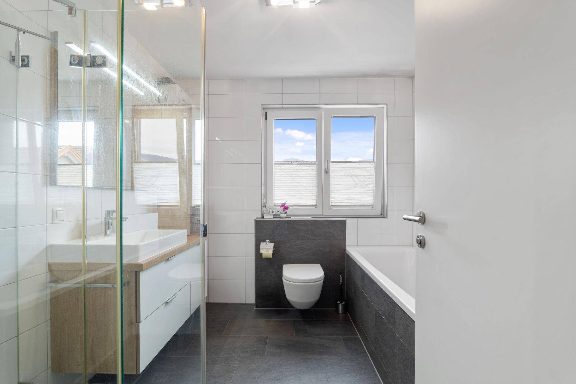 Helles Badezimmer mit Fenster, Badewanne, Dusche und modernem Waschtisch in zeitgemäßem Design.