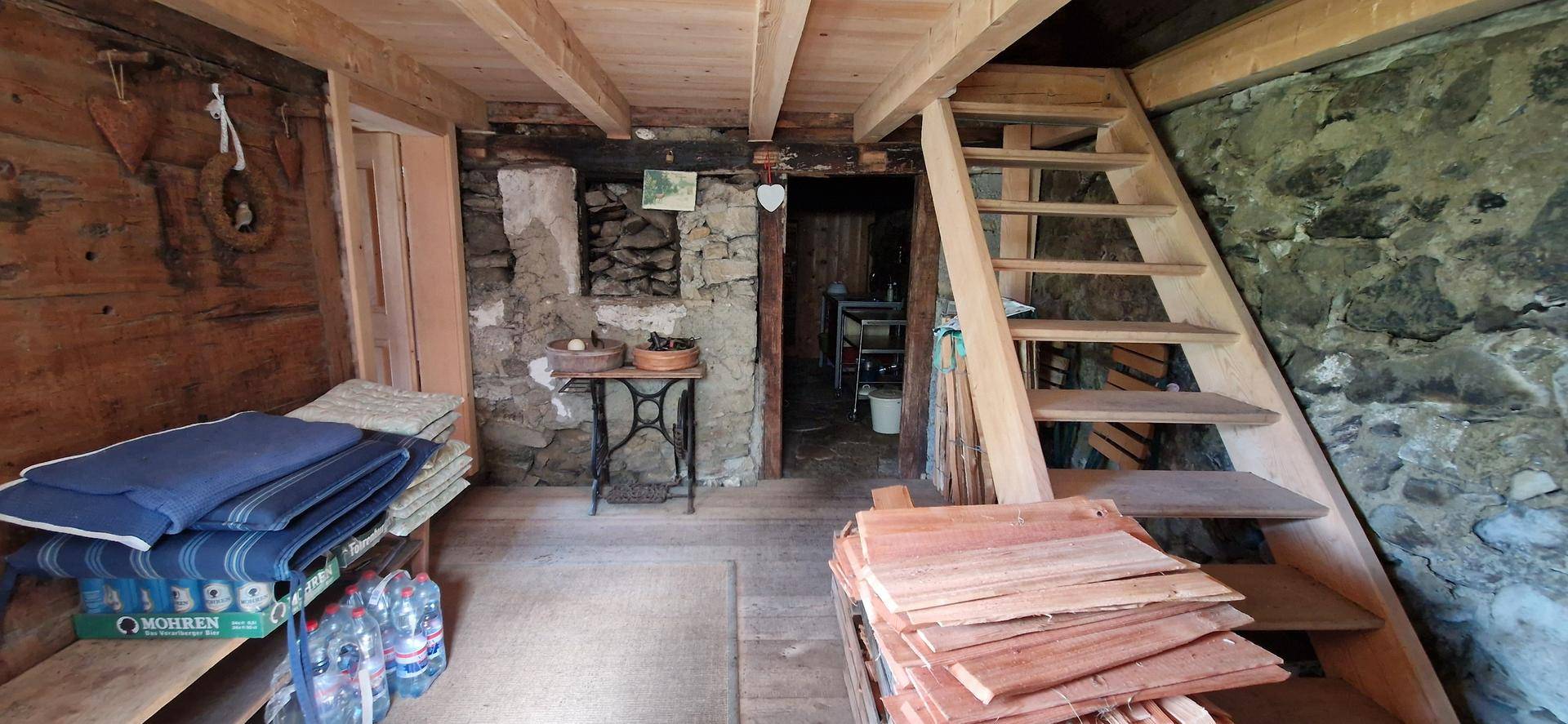 Rustikaler Abstellraum mit Steinfundament, Holztreppe und gelagerten Materialien.