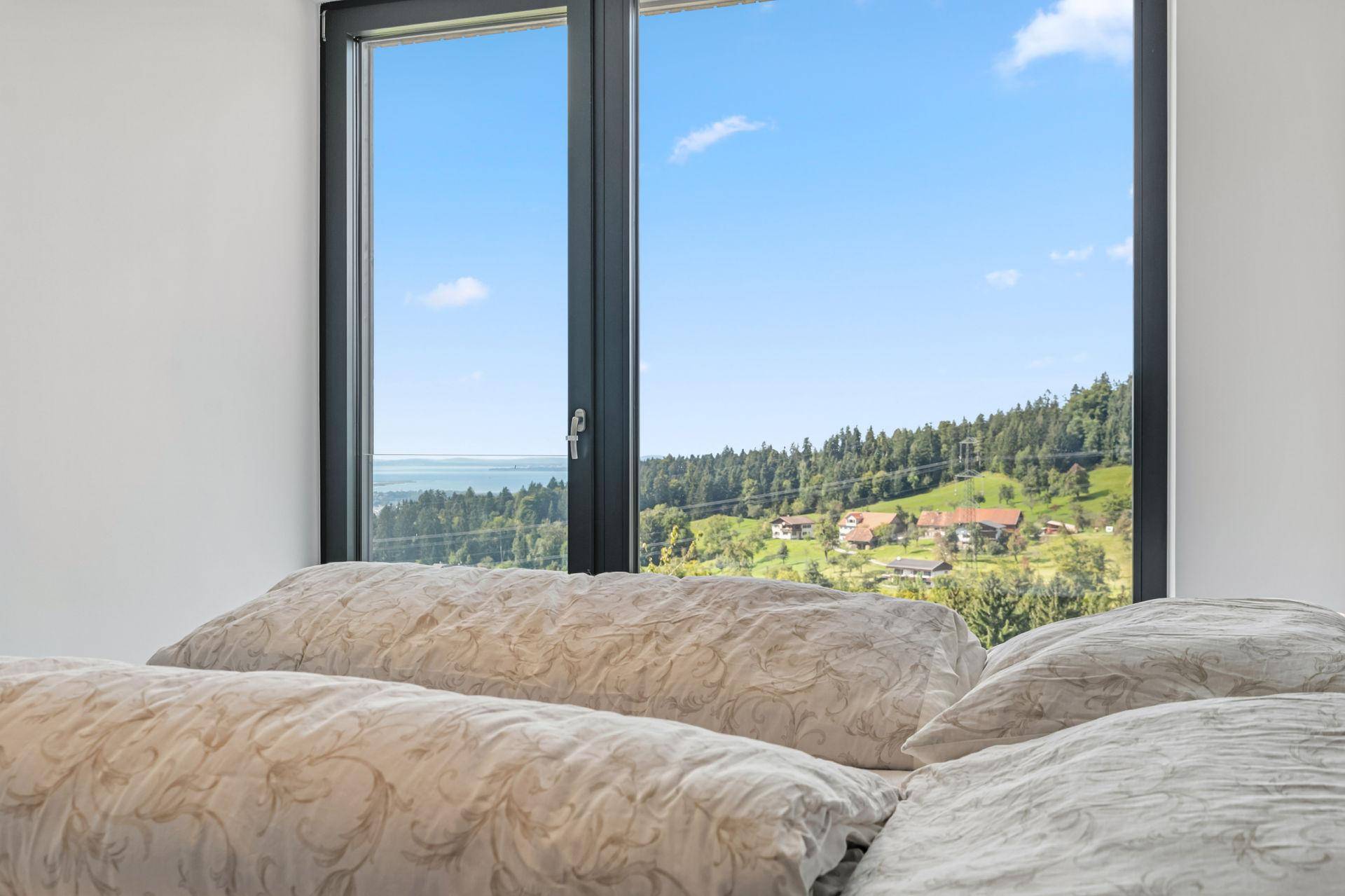 Schlafzimmer mit direktem Blick aus dem Fenster auf die grüne Landschaft und den fernen See.