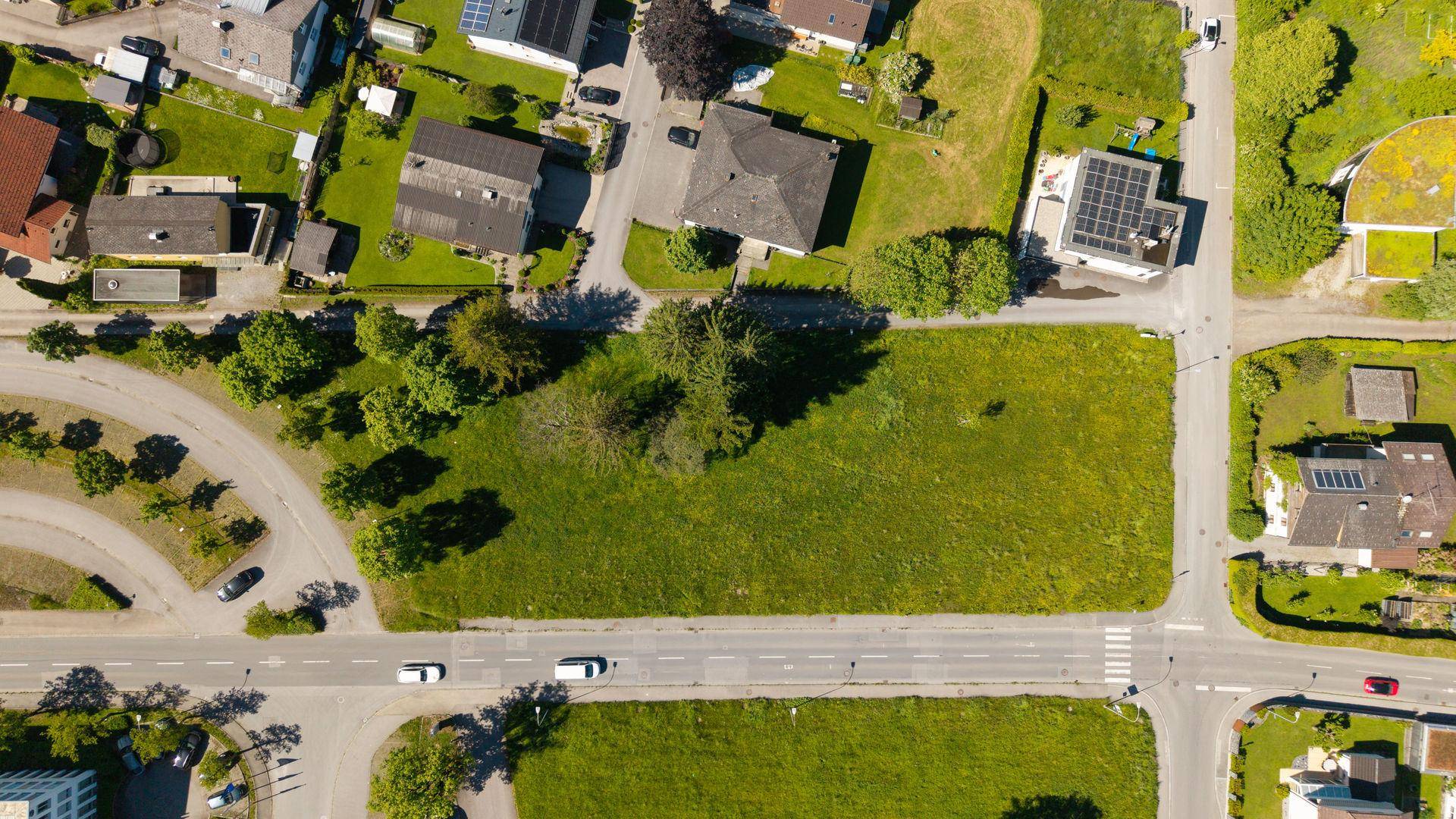 Draufsicht auf ein grünes Grundstück, umgeben von Straßen und einzelnen Bäumen.