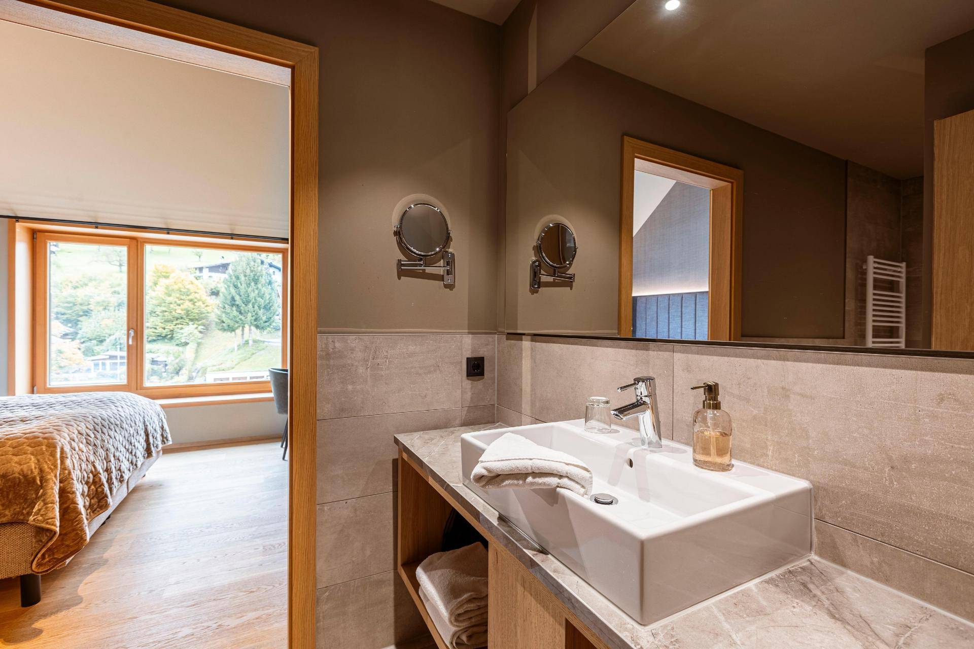 Badezimmer mit modernem Waschbecken, großem Spiegel und Zugang zum Schlafzimmer.