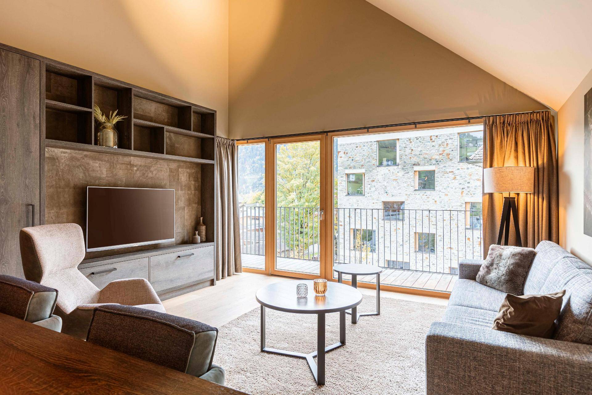 Gemütliches Wohnzimmer mit Sofa, Teppich und Zugang zu einem Balkon mit Bergblick.