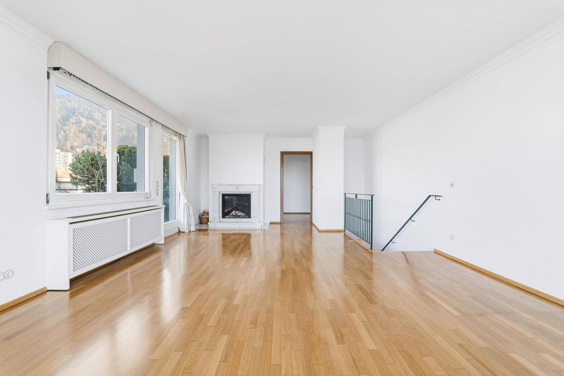 Geräumiges Wohnzimmer mit hellem Parkettboden, einem eleganten Kamin und viel Tageslicht.