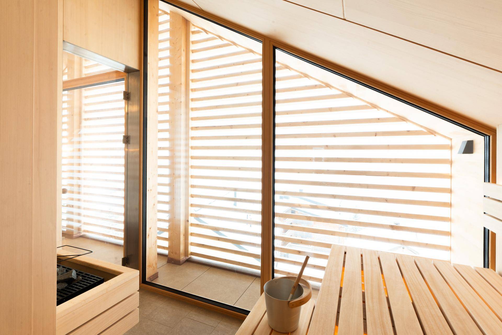 Helle Sauna mit Holzbänken, großen Fenstern und Blick auf die verschneite Landschaft.