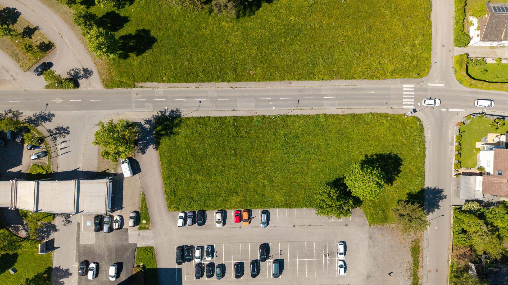 Draufsicht auf ein unbebautes Grundstück, umgeben von Straßen und einem Parkplatz.