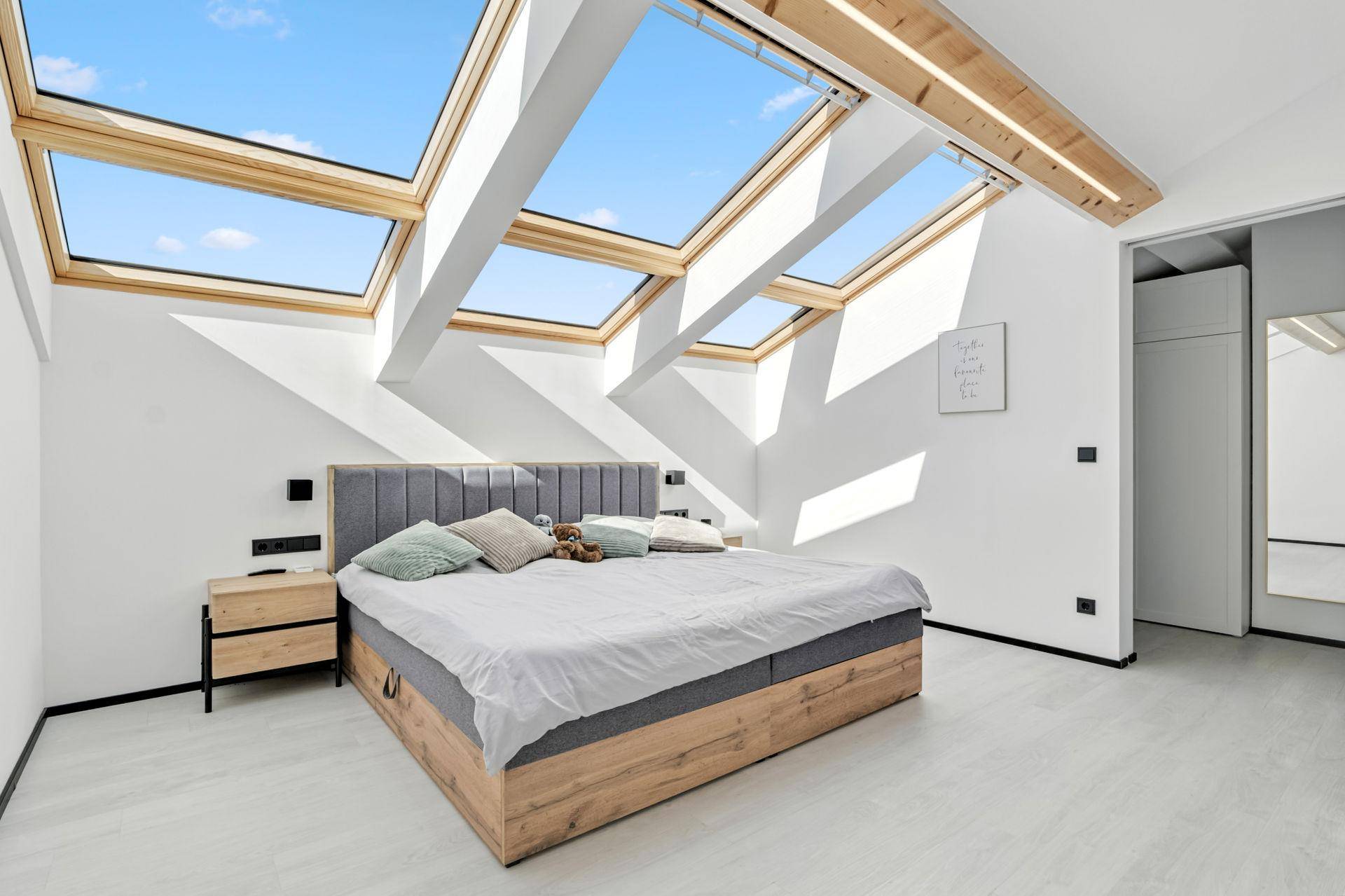Helles Schlafzimmer mit großem Bett, Holzmöbeln und mehreren Dachfenstern für viel Tageslicht.