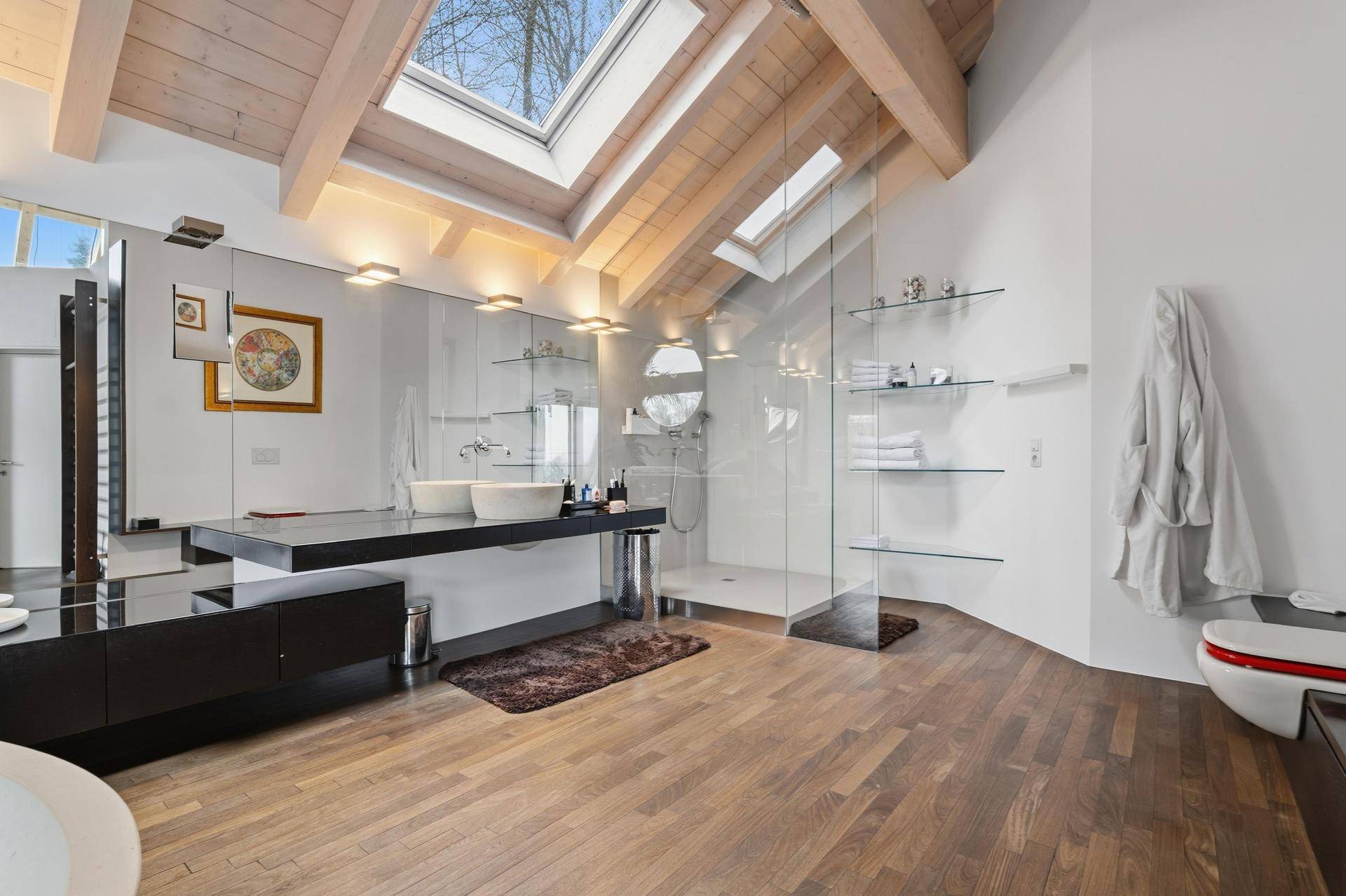 Geräumiges Badezimmer mit begehbarer Dusche, Doppelwaschbecken und Holzboden unter einem Dachfenster.