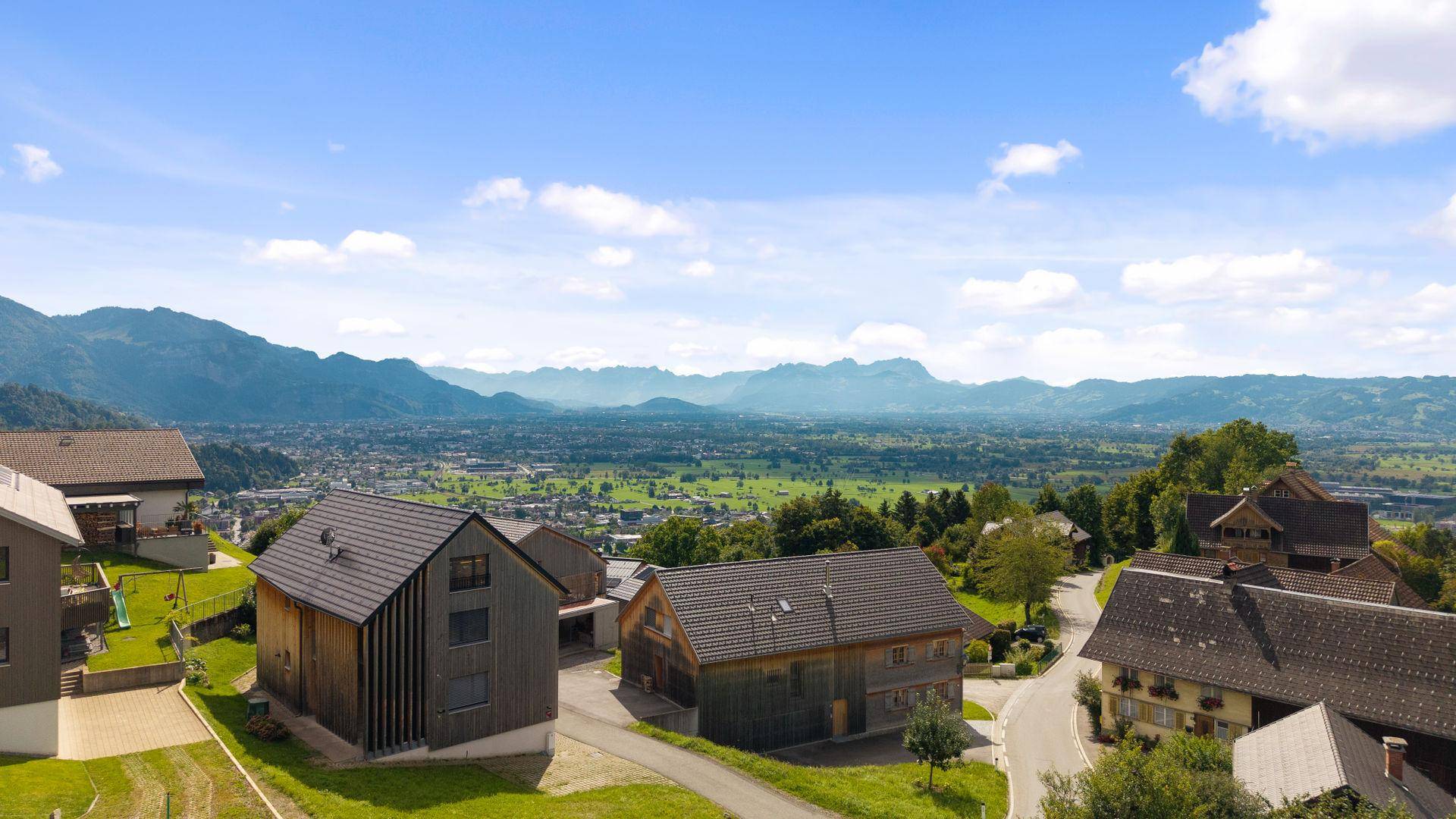 Panoramablick auf eine ländliche Siedlung mit traditionellen Häusern und majestätischen Bergen im Hintergrund.