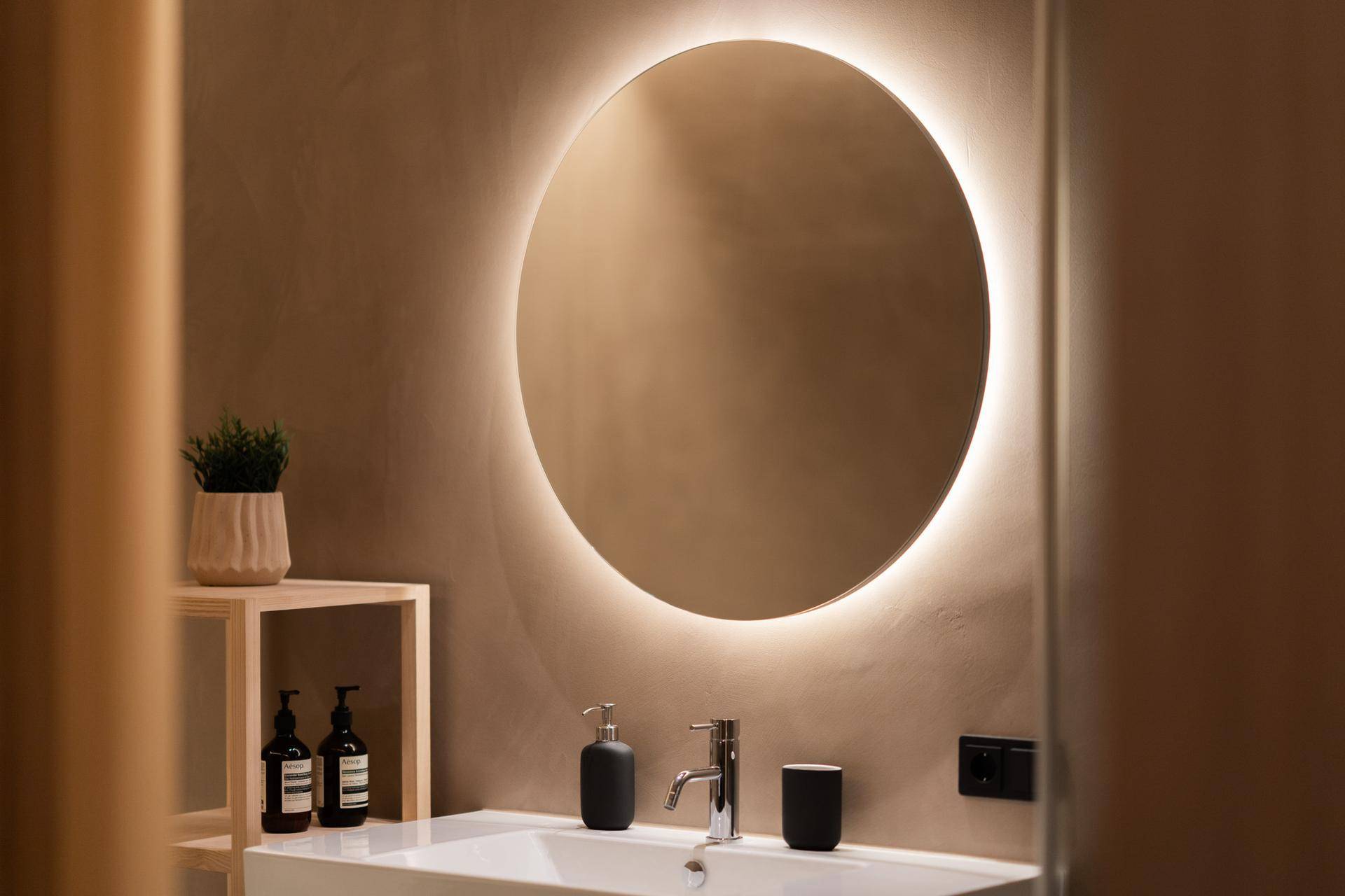 Modernes Badezimmer mit beleuchtetem Rundspiegel, elegantem Waschbecken und minimalistischem Design.