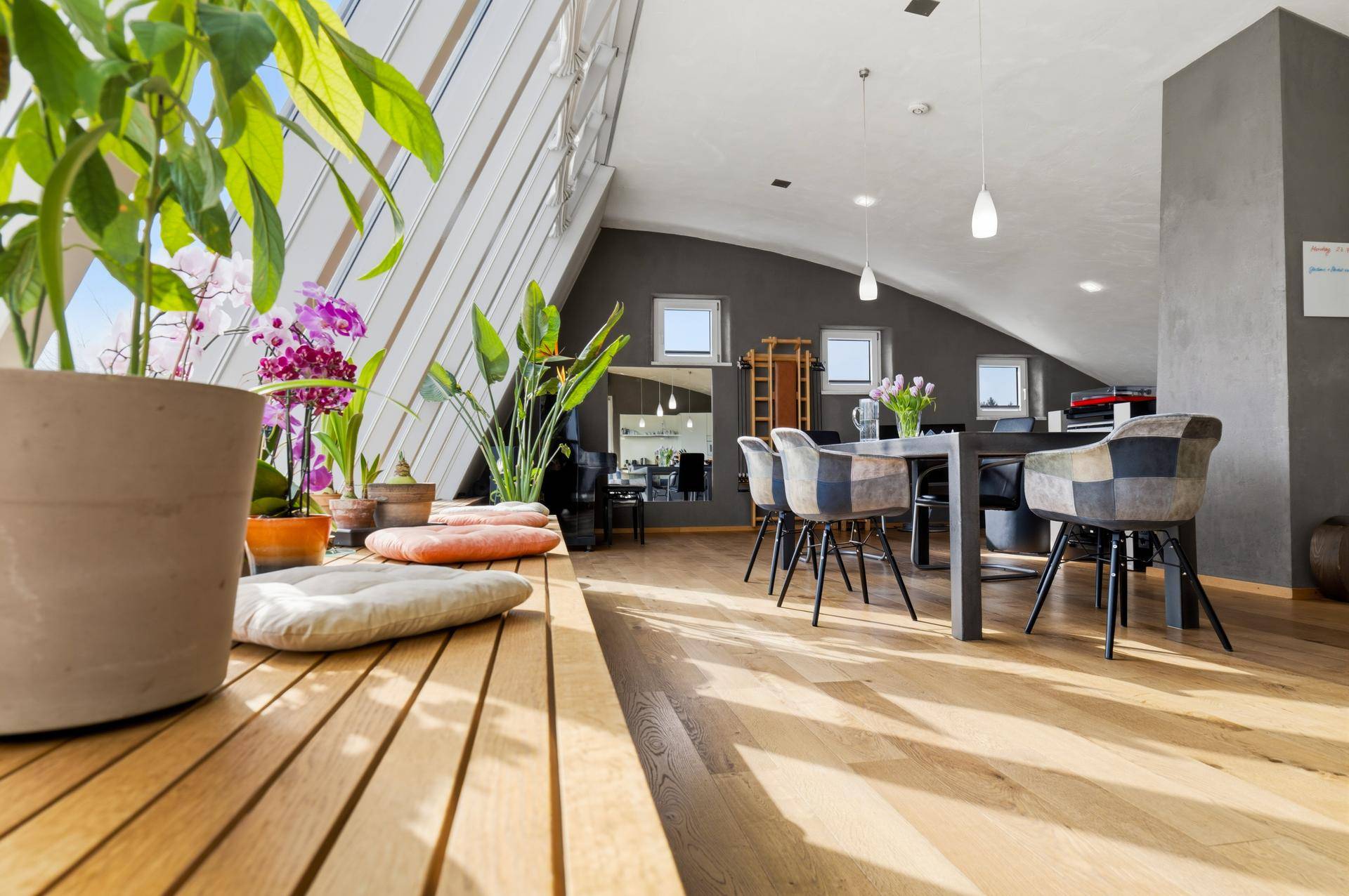 Heller Wohnbereich mit schrägen Wänden, großen Fenstern und Holzboden, ideal für Pflanzenliebhaber.