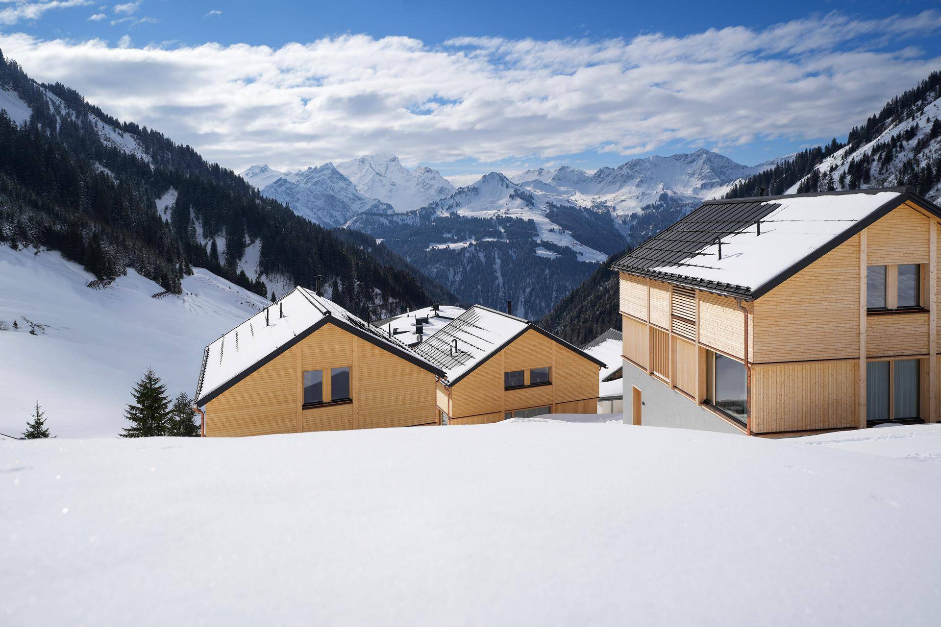 Moderne Holzhäuser in einer tief verschneiten Berglandschaft mit majestätischem Alpenpanorama.