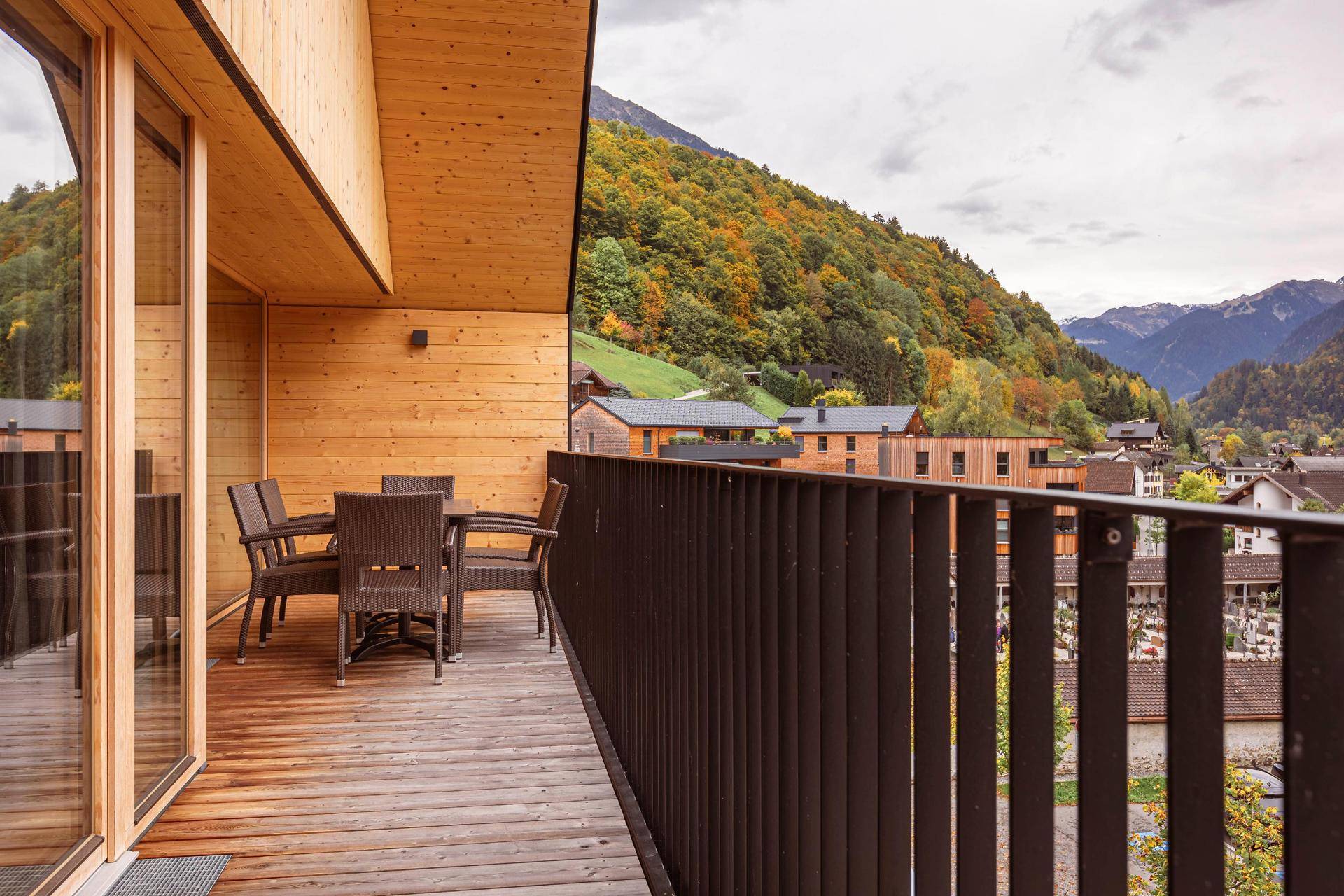 Geräumiger Balkon mit Holzboden, Esstisch und Stühlen, umgeben von Bergen.