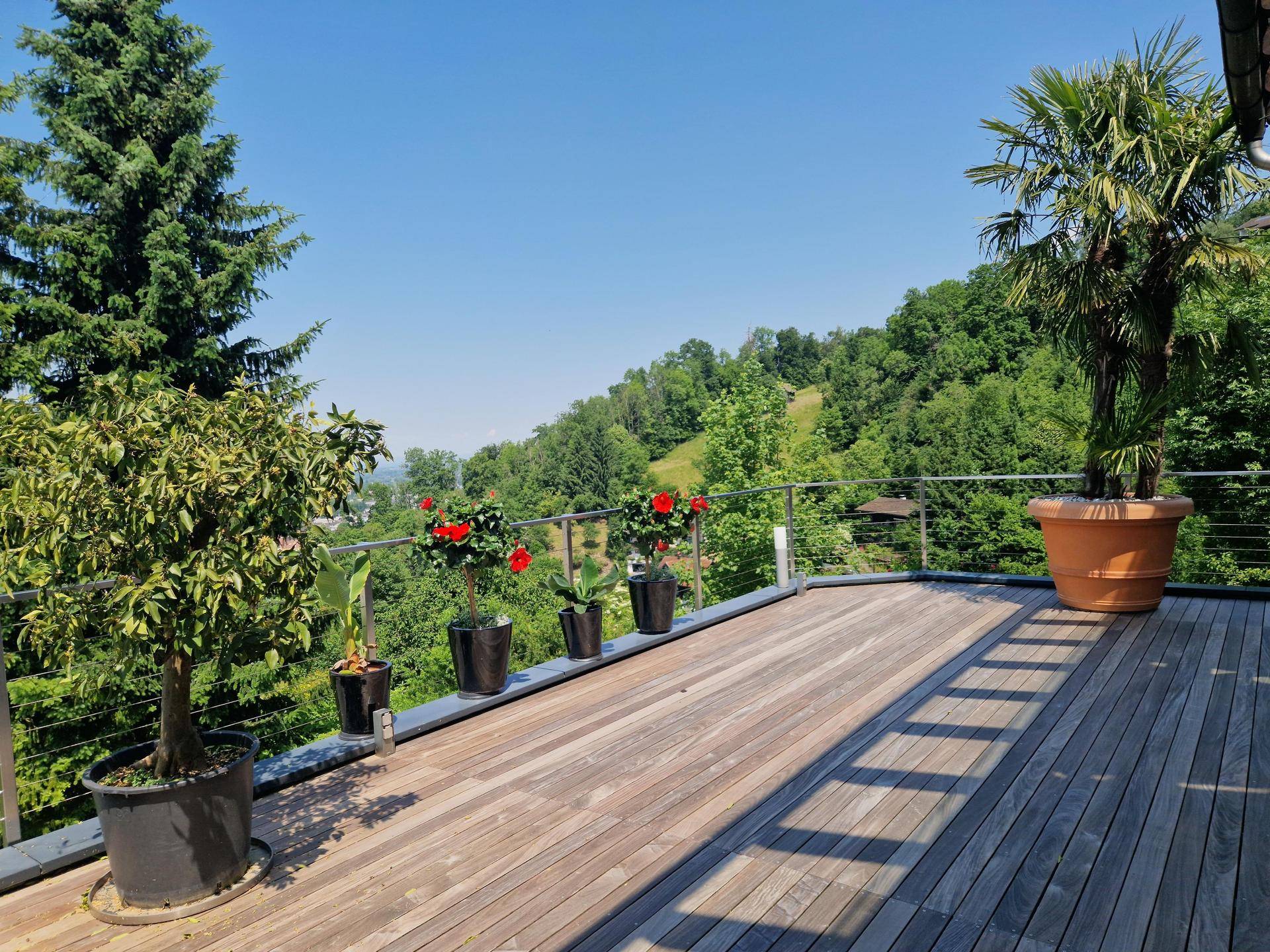 Geräumige Holzterrasse mit Pflanzen und einem weiten Blick auf die grüne Hügellandschaft.