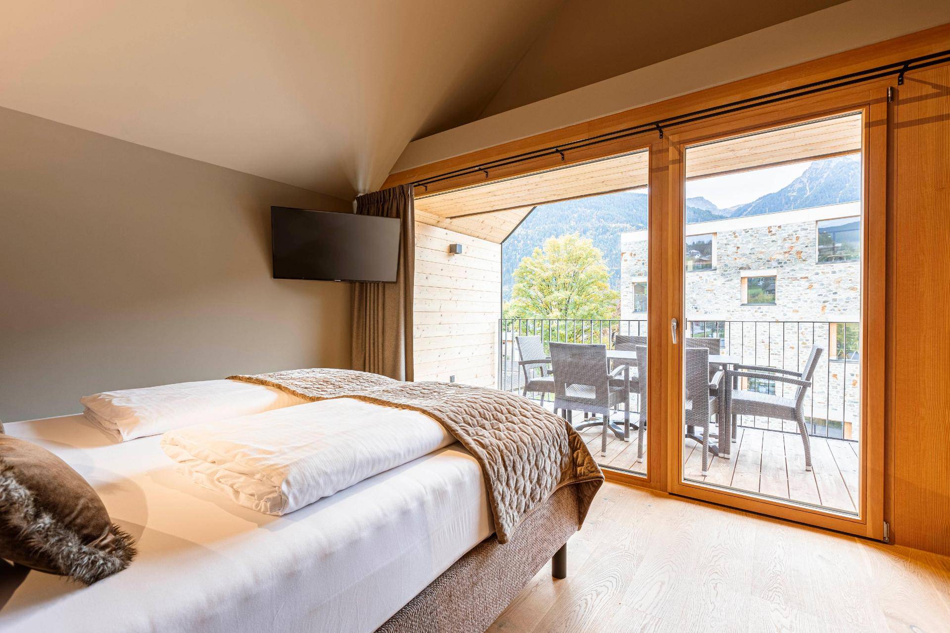 Schlafzimmer mit Doppelbett, Holzboden und direktem Zugang zum Balkon mit Bergblick.