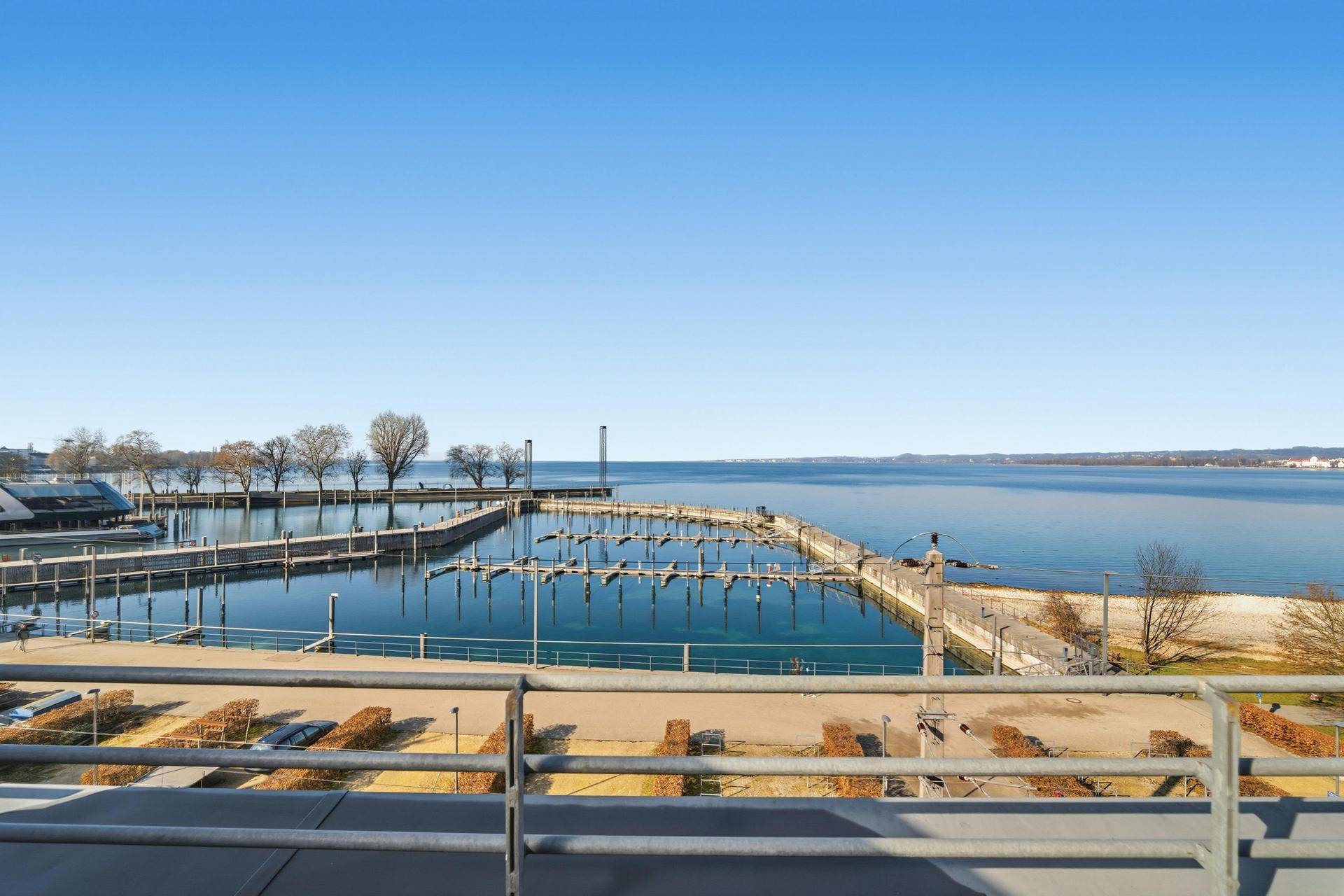 Weitblick vom Balkon auf den Yachthafen und das ruhige Wasser des Sees unter blauem Himmel.