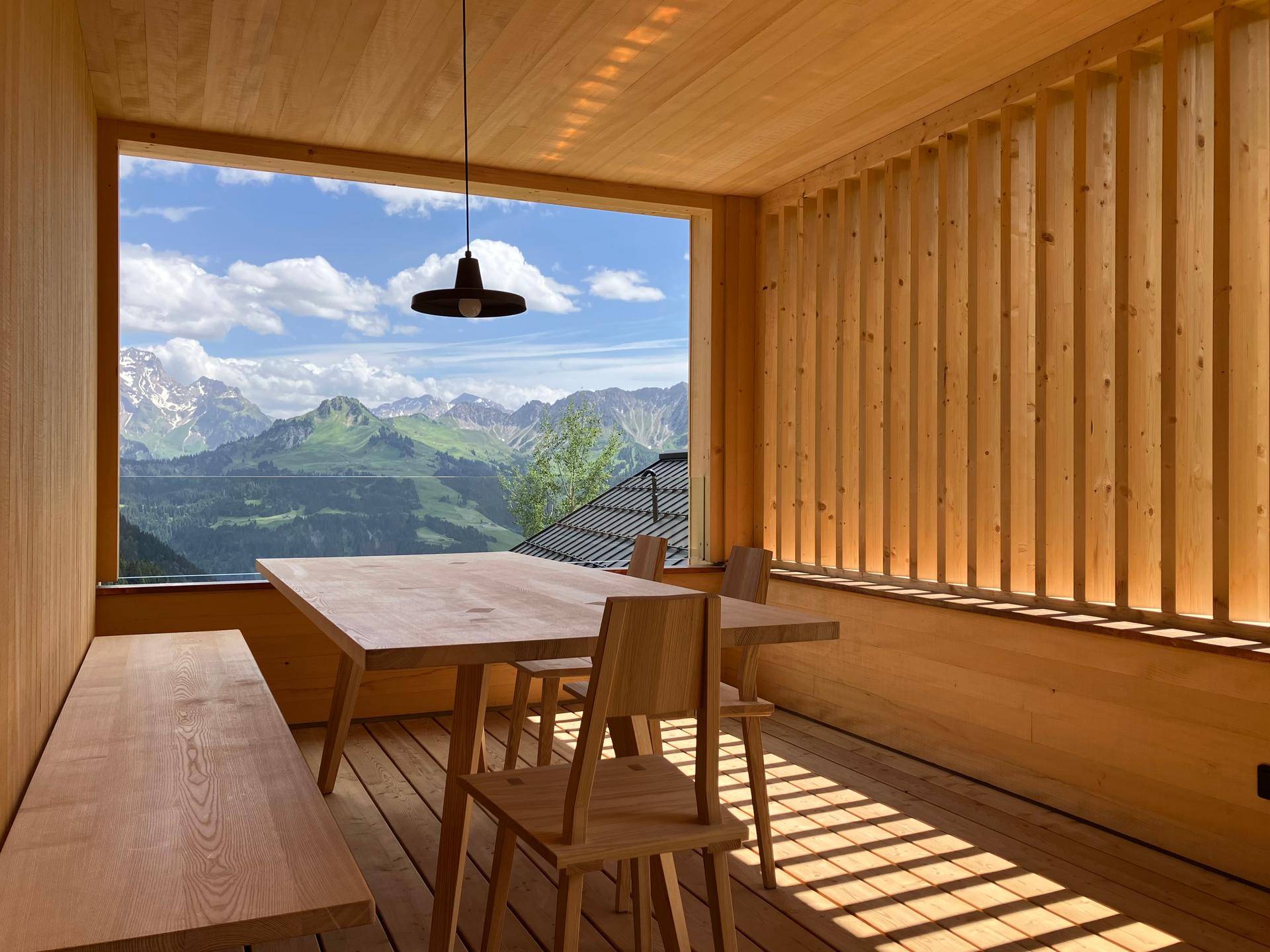 Heller Essbereich mit Holztisch und Sitzbank, großen Fenstern und beeindruckendem Bergblick.