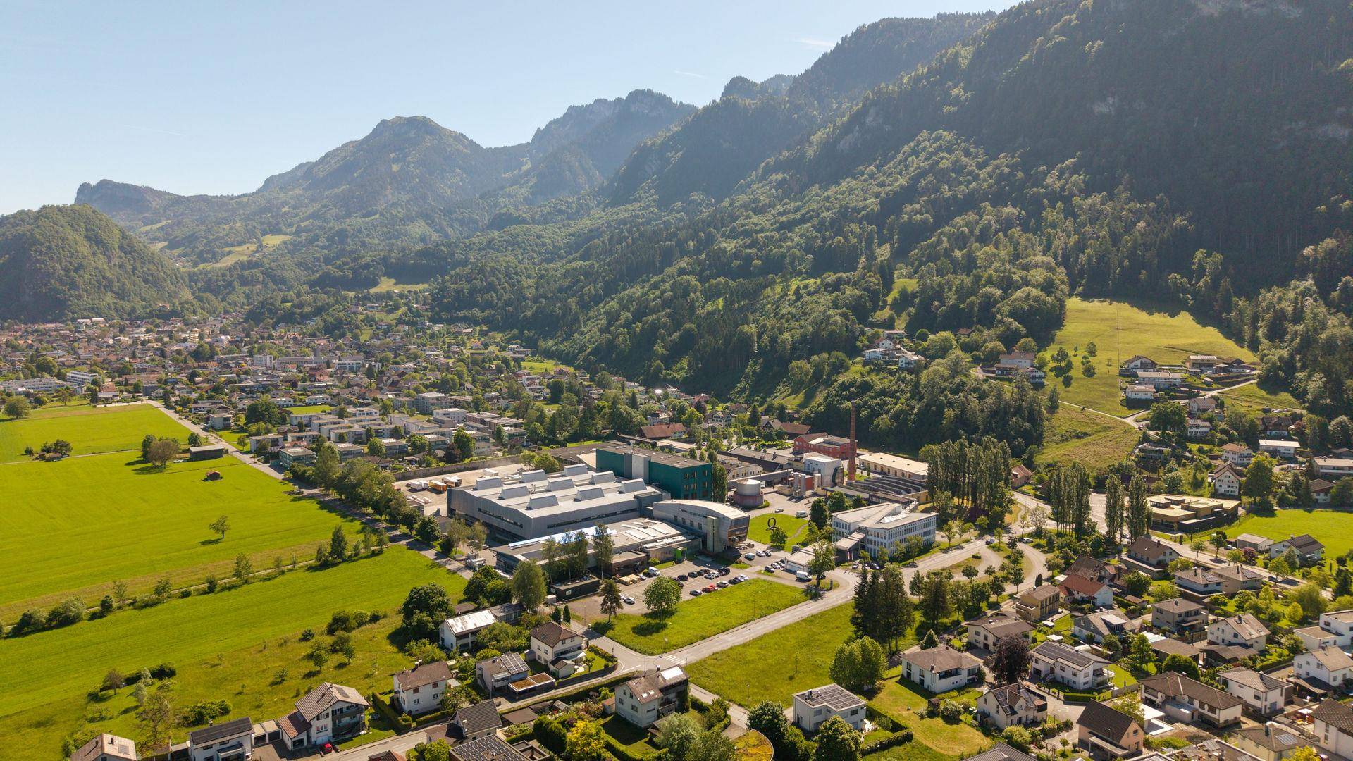 Luftaufnahme einer Ortschaft am Fuße eines bewaldeten Berges mit Wohn- und Gewerbegebieten.