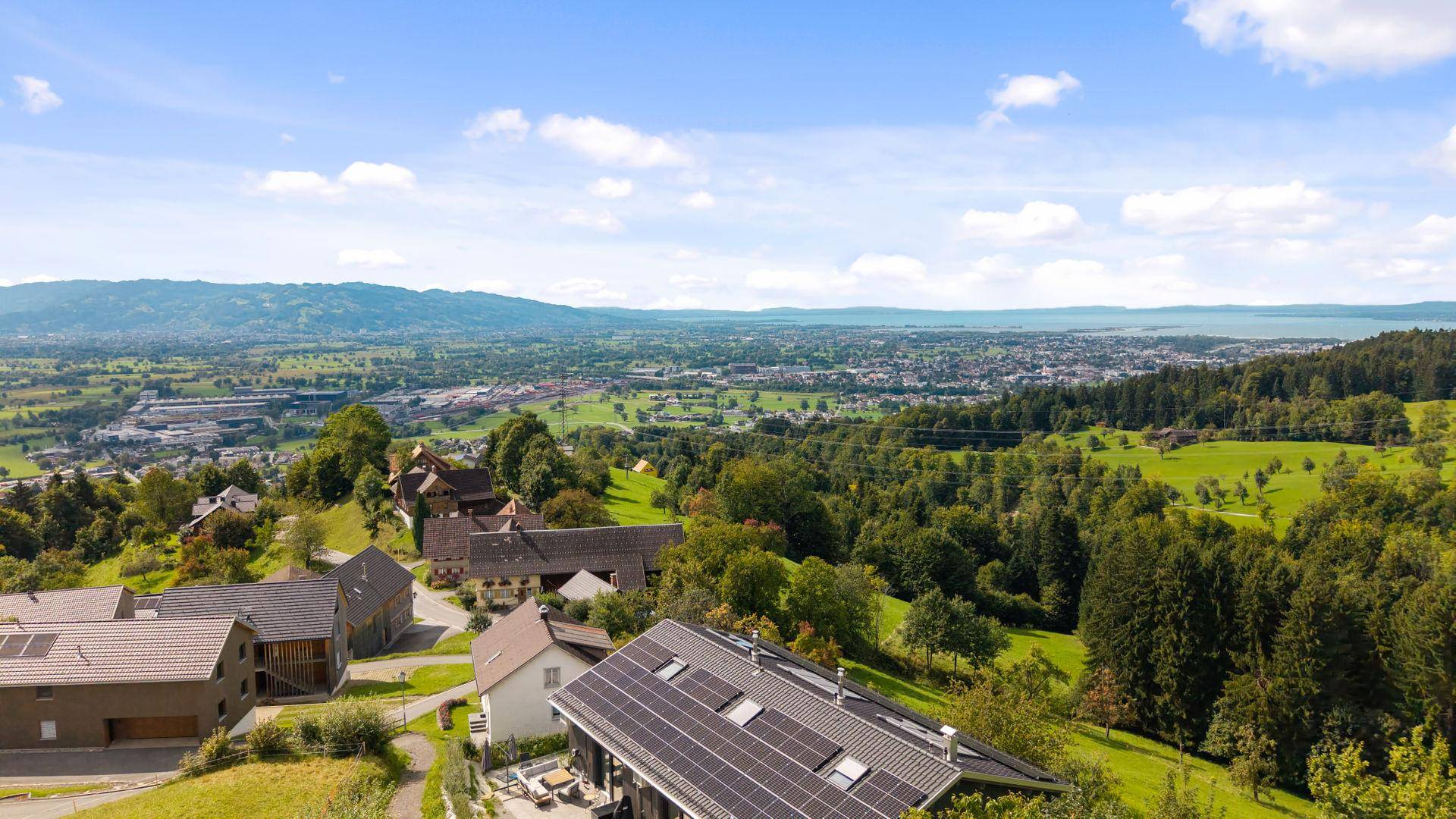 Luftaufnahme eines modernen Hauses mit Photovoltaikanlage auf dem Dach in grüner Hanglage.