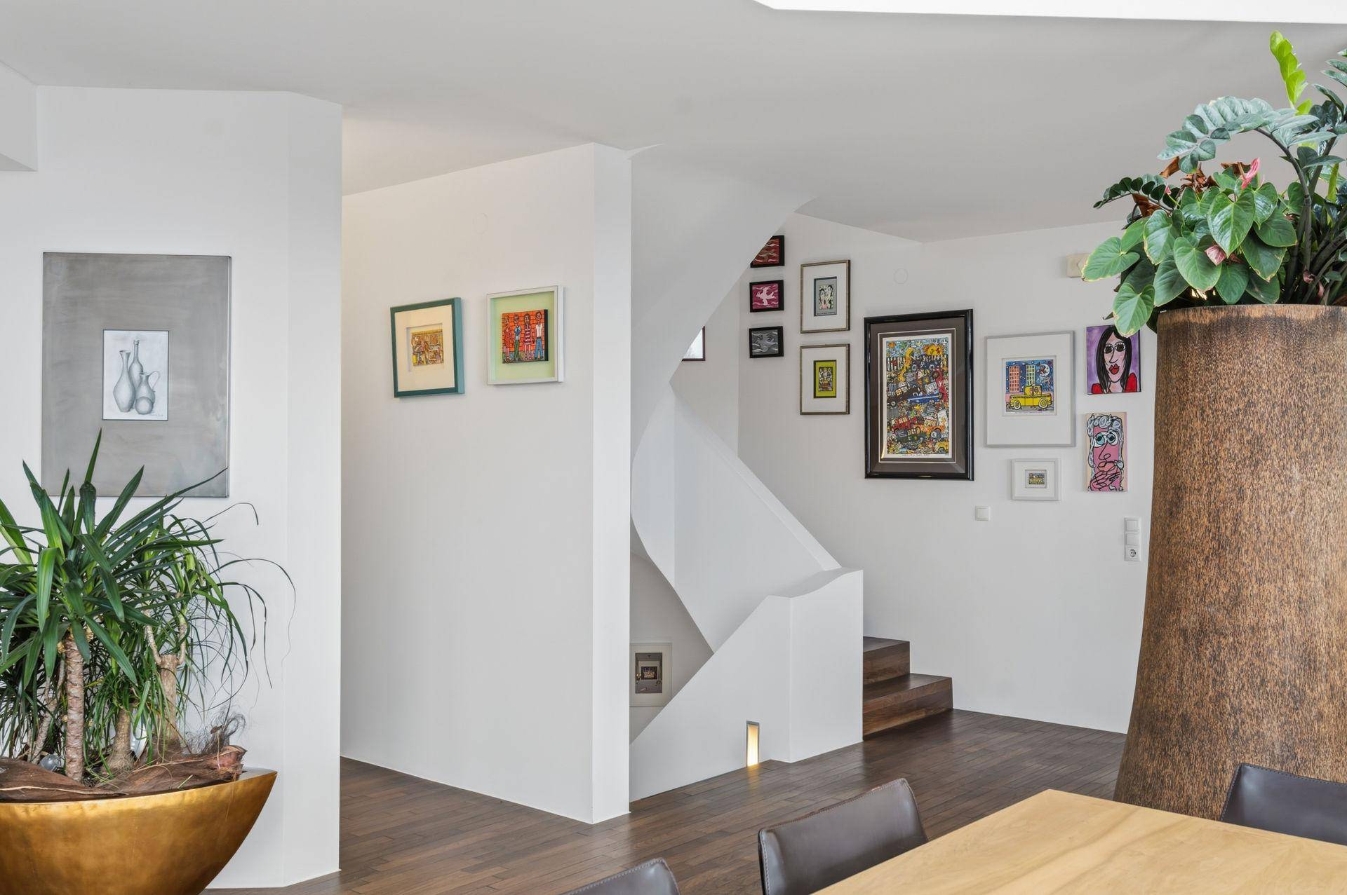 Moderner Treppenaufgang mit weiß gestrichenen Wänden, Holzboden und einer Galerie von Kunstwerken.
