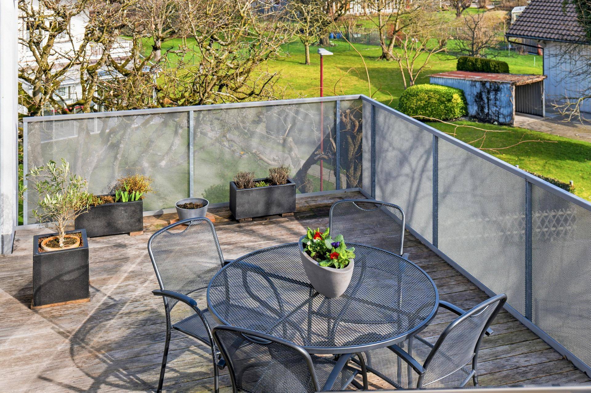 Sonniger Balkon mit Holzboden und Metallgeländer, ausgestattet mit einem kleinen Sitzbereich.