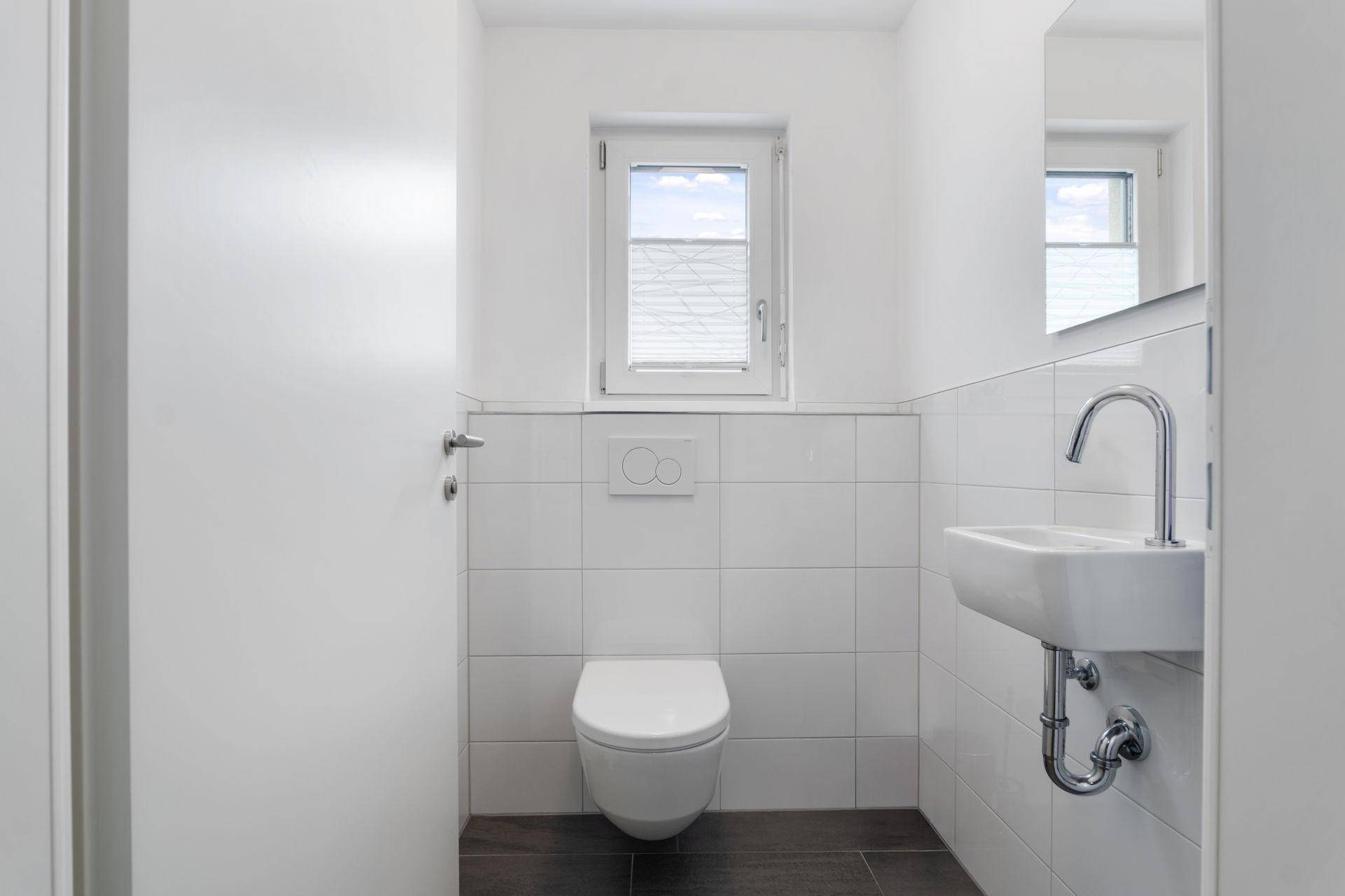 Kleines Gäste-WC mit Fenster, Wand-WC und modernem Handwaschbecken in schlichtem Design.