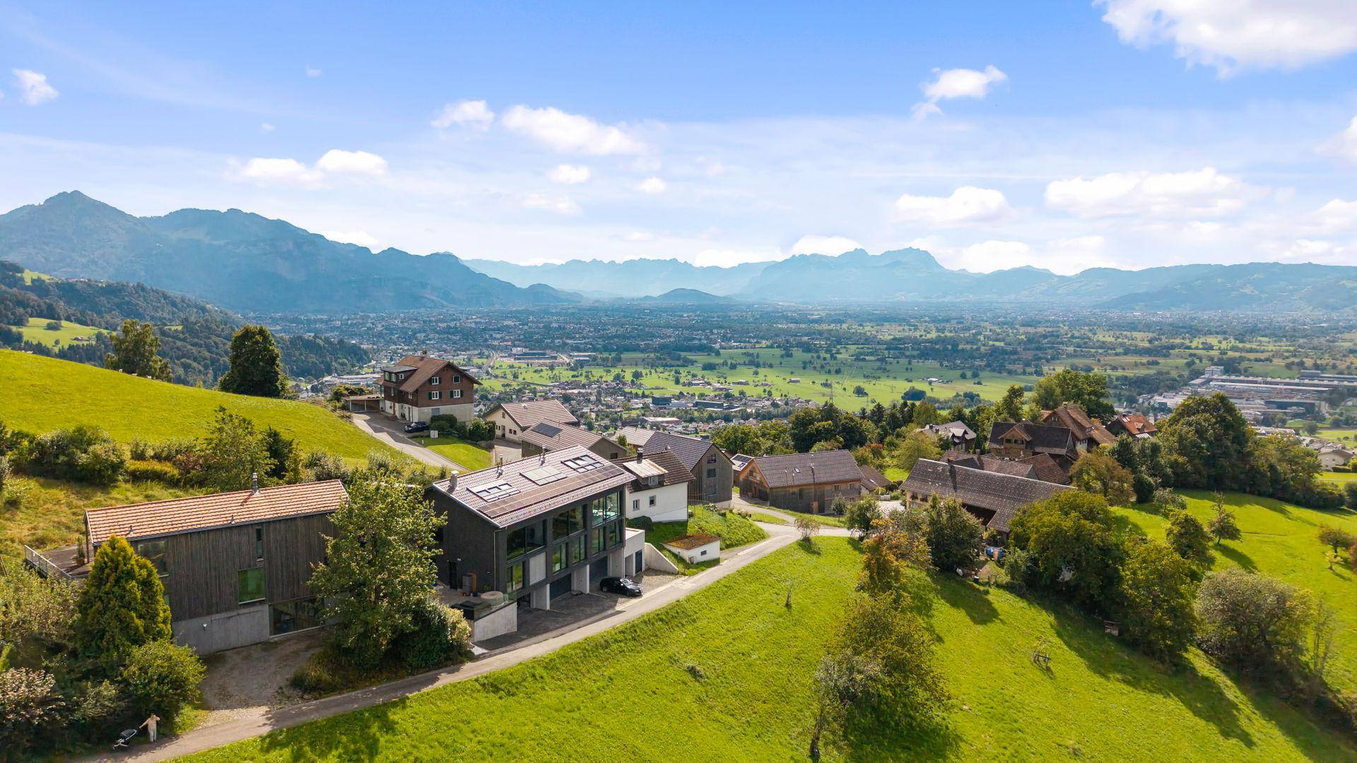 Weitläufige Luftaufnahme des Anwesens mit moderner Architektur und Bergblick in grüner Umgebung.