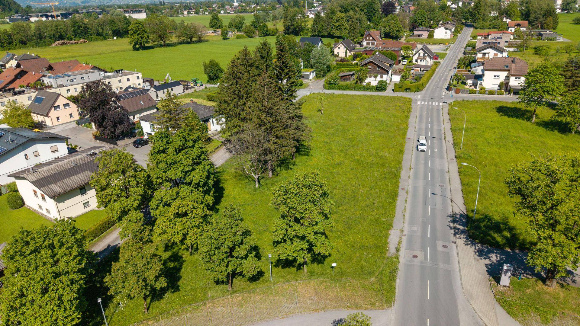 Weitläufige Luftaufnahme eines Grundstücks mit umliegenden Häusern, Straßen und grüner Landschaft im Hintergrund.