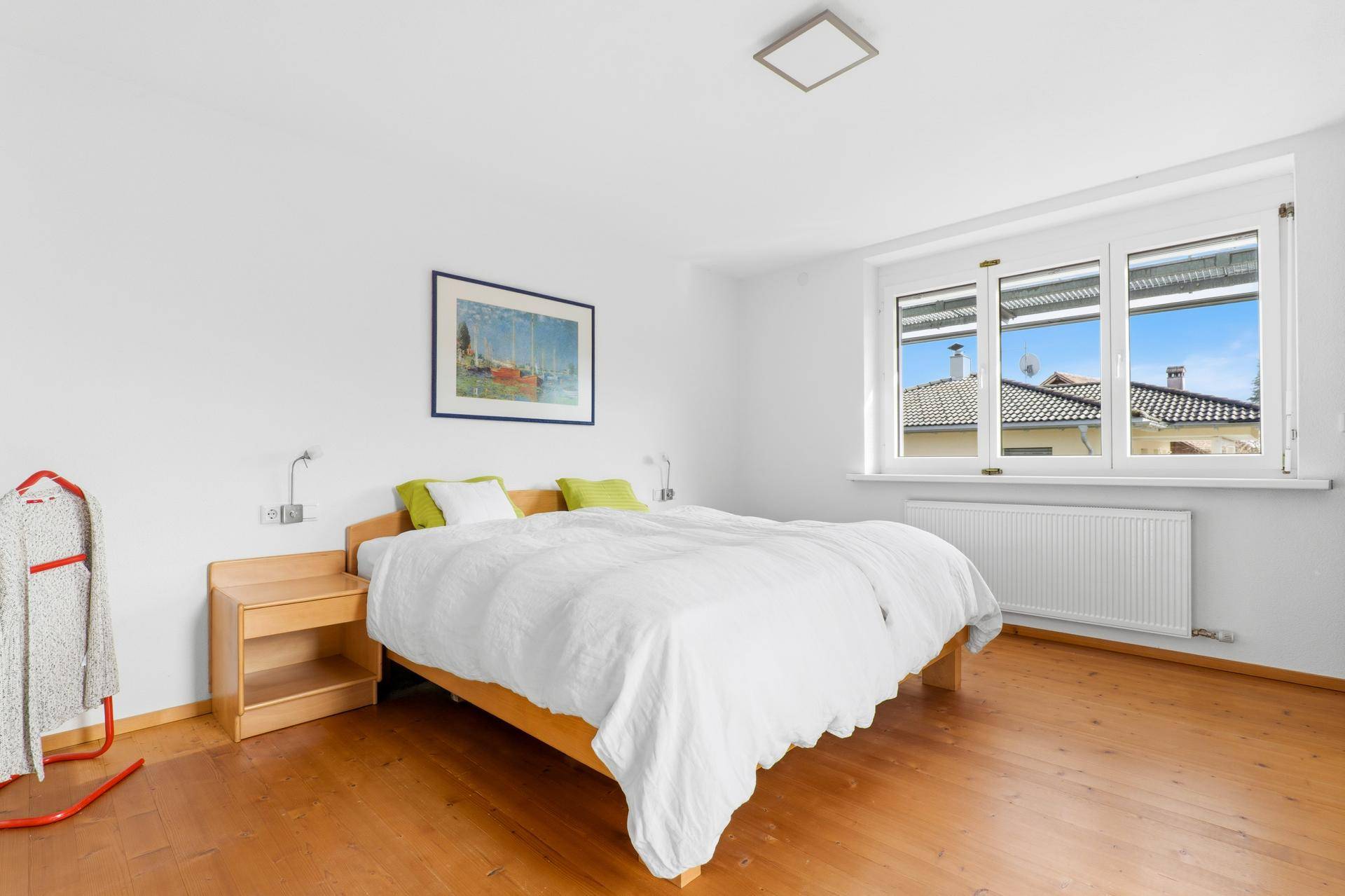 Helles Schlafzimmer mit Holzboden, weiß gestrichenen Wänden und großem Fenster mit Ausblick.