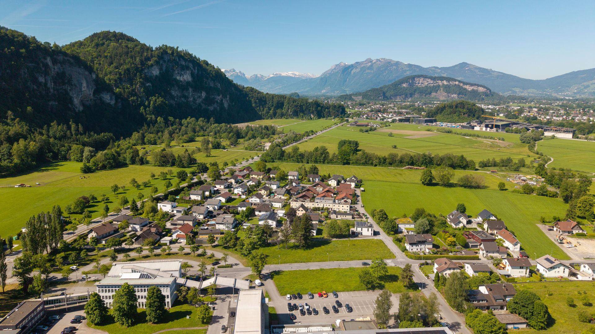 Panoramablick aus der Luft über eine Siedlung mit weiten Feldern und schneebedeckten Bergen.