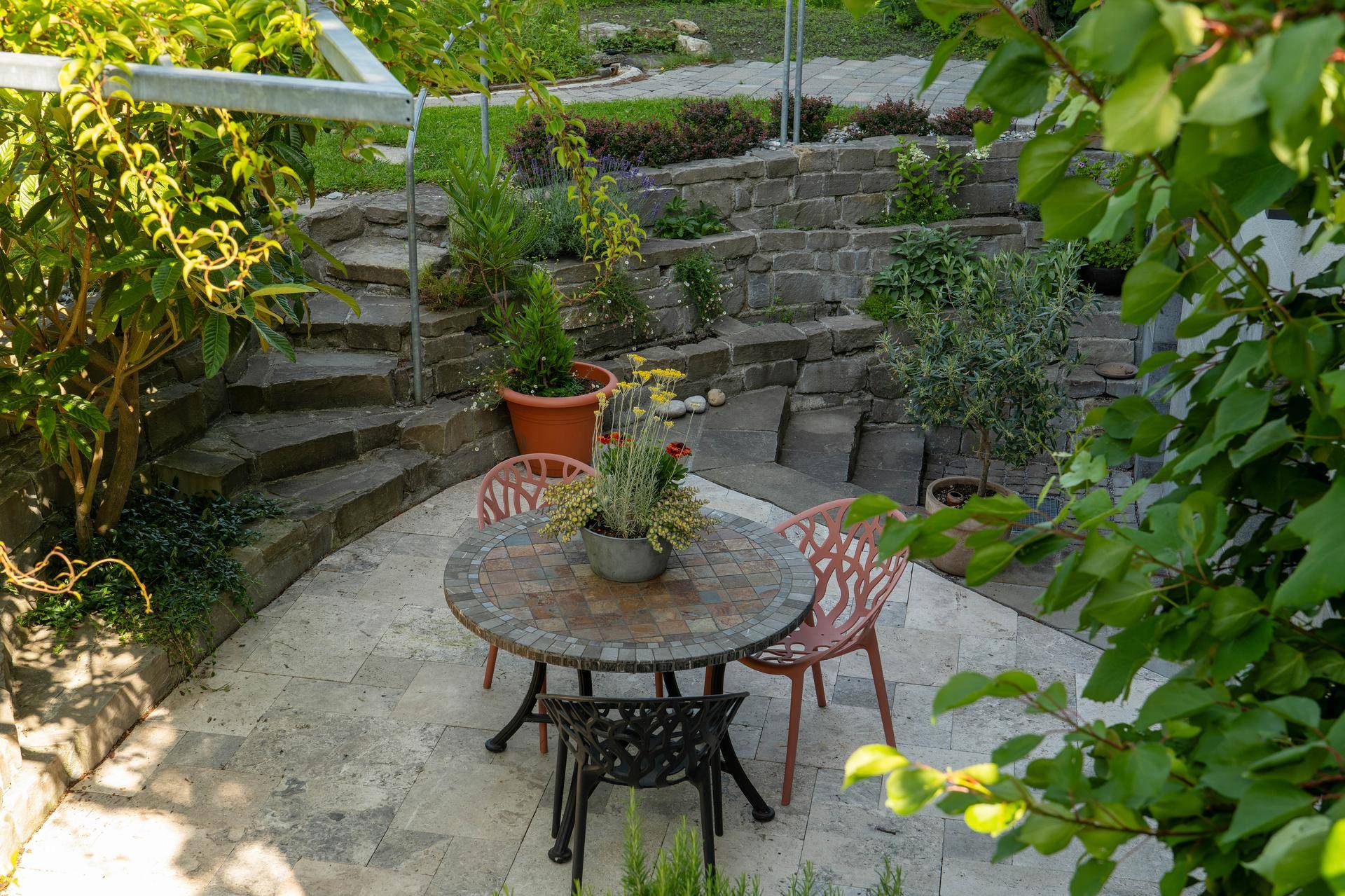 Gemütliche Terrasse mit Mosaiktisch und Stühlen, umgeben von einer Steintreppe und Pflanzen.